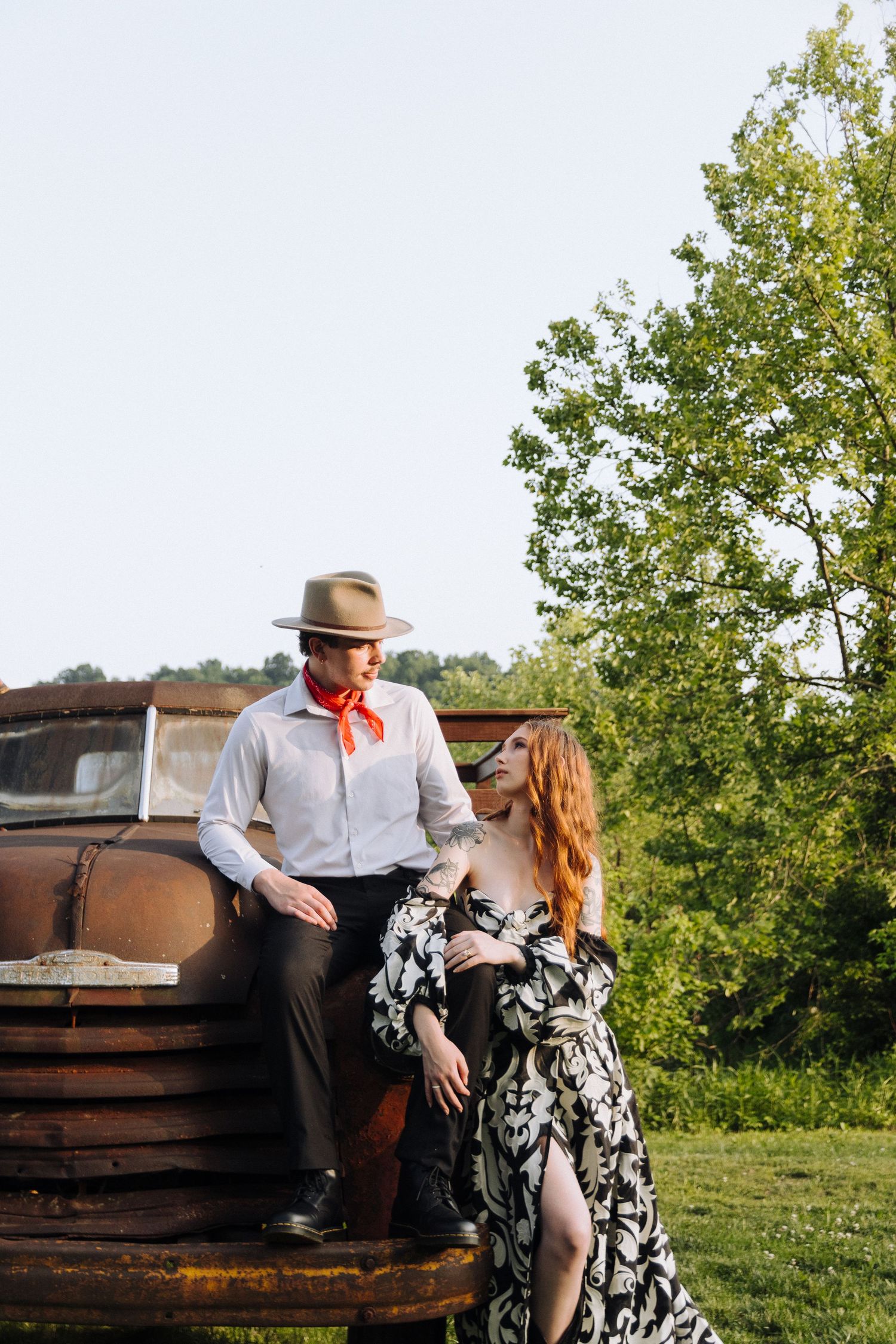 Couple sitting together on a rustic bench outdoors with trees and grass in a romantic countryside setting.