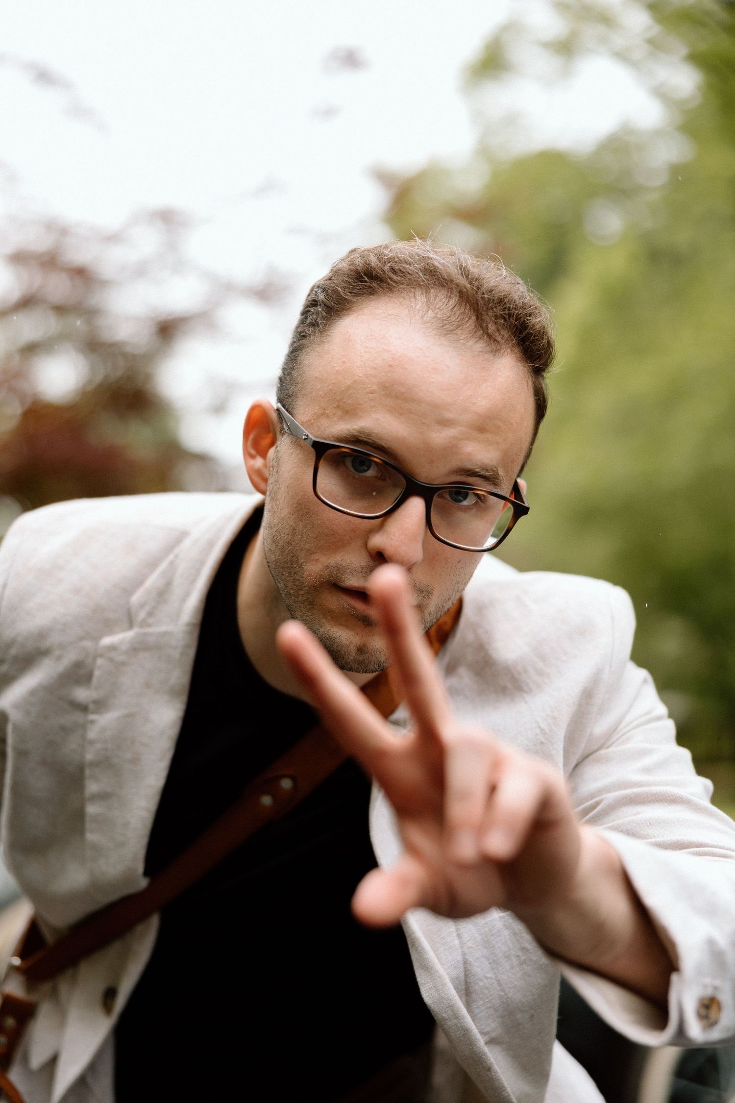 Portrait series showing a person in glasses and white shirt making peace signs while playfully posing outside.