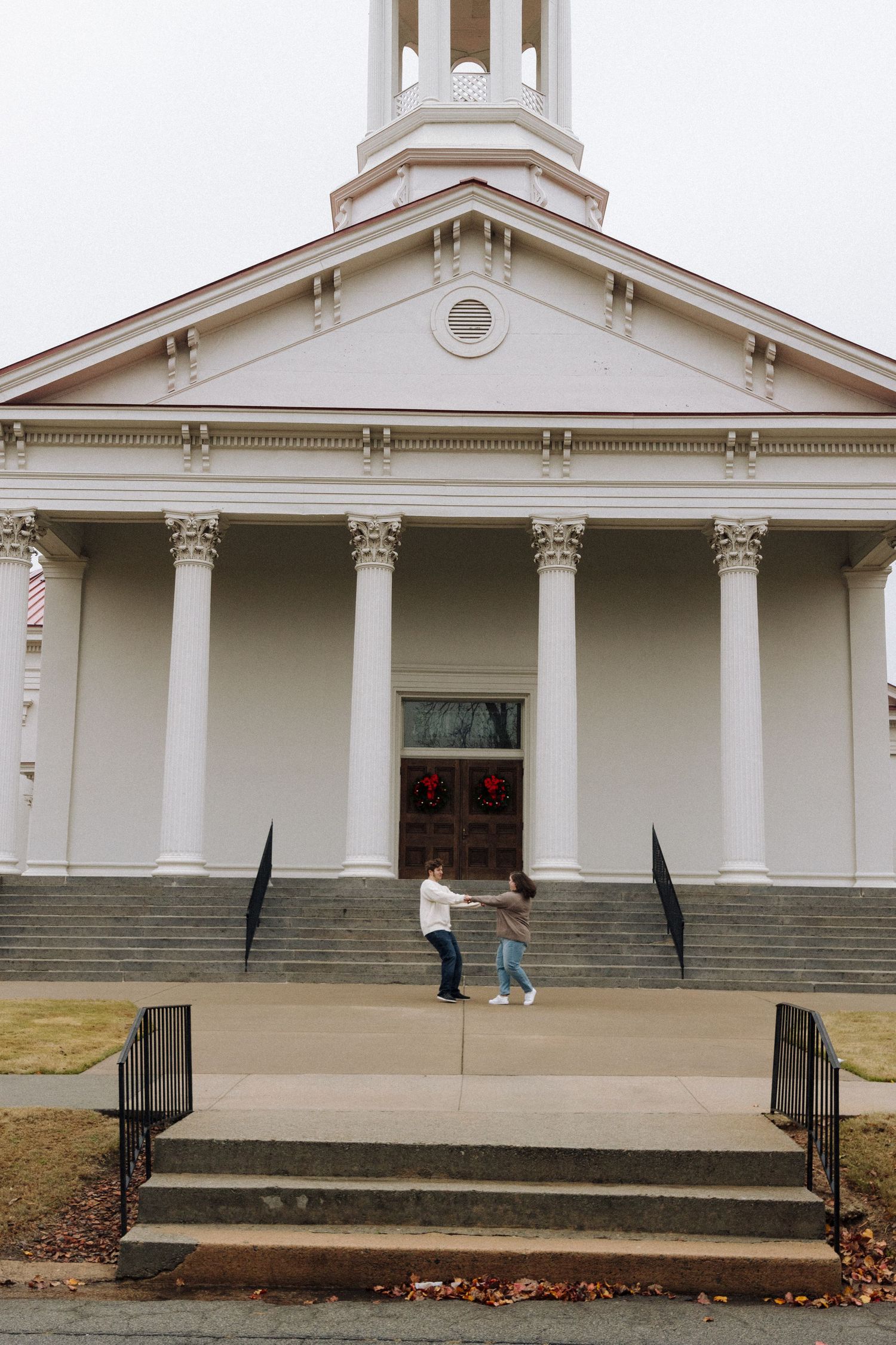 Classic white church building with tall columns and pediment entrance, featuring visitors ascending stone steps.