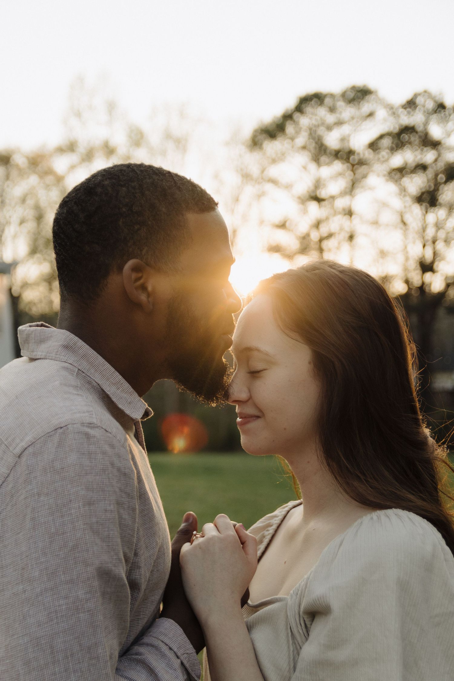 Loving couple sharing an intimate moment in golden sunset light with trees silhouetted in background.