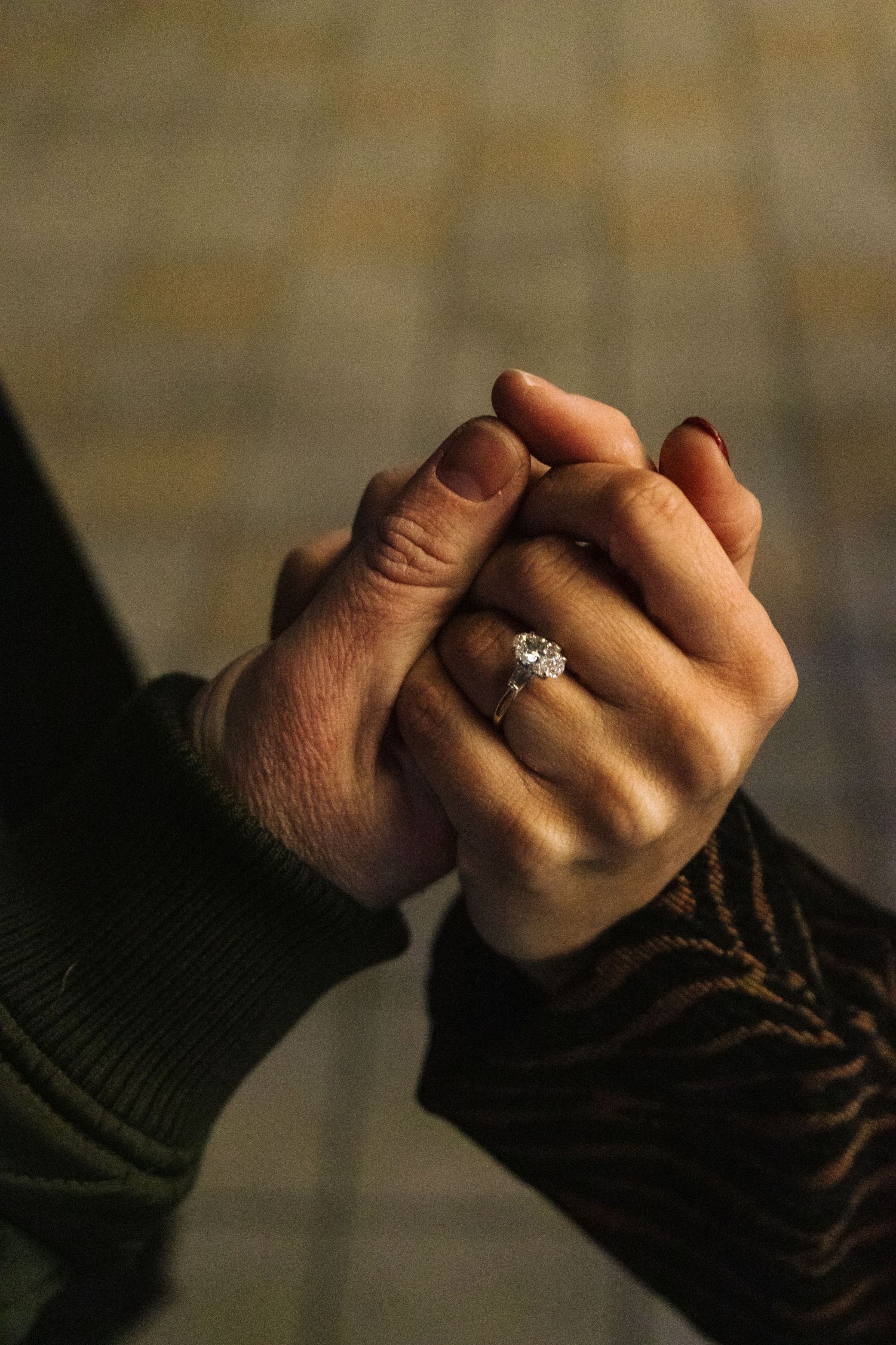 Two hands clasped together in an intimate moment, with a sparkling engagement ring visible on one finger.