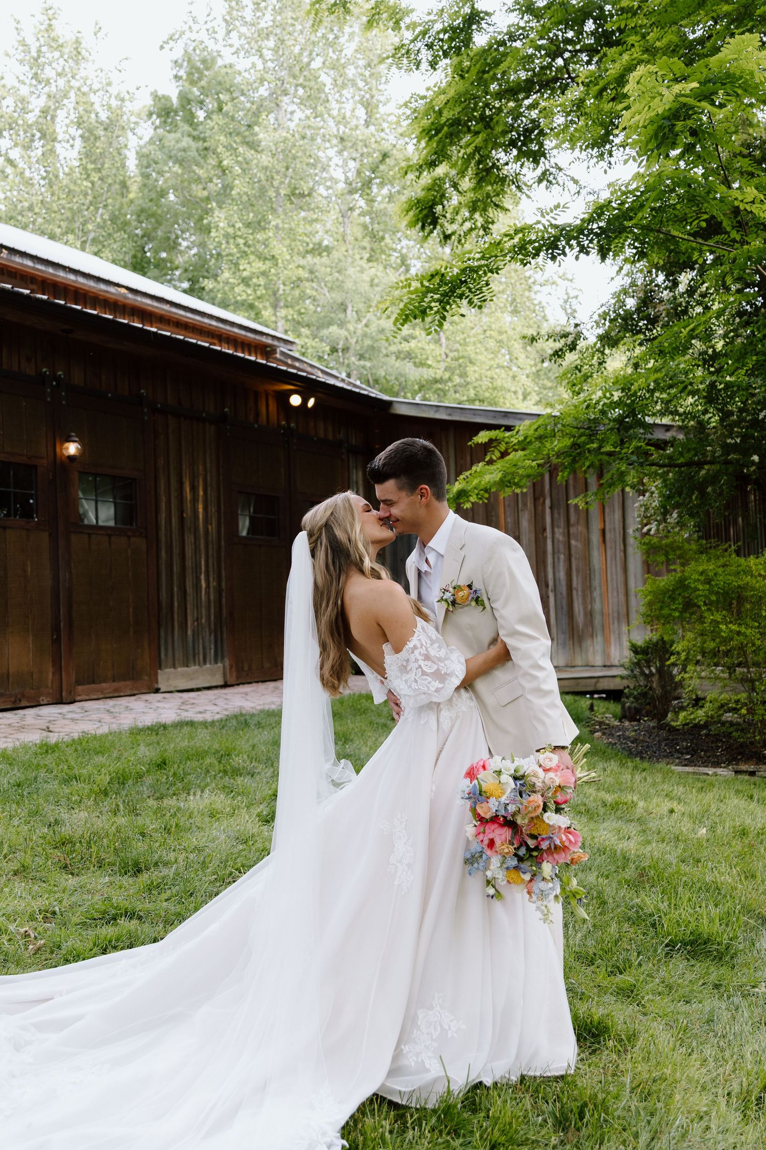 Bride and groom sharing a romantic moment outdoors near a rustic barn, bride holding a colorful bouquet.