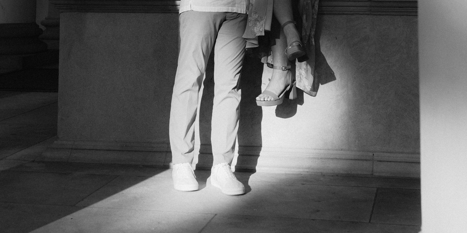 Black and white photo showing the legs and feet of people walking down a brightly illuminated hallway or corridor.