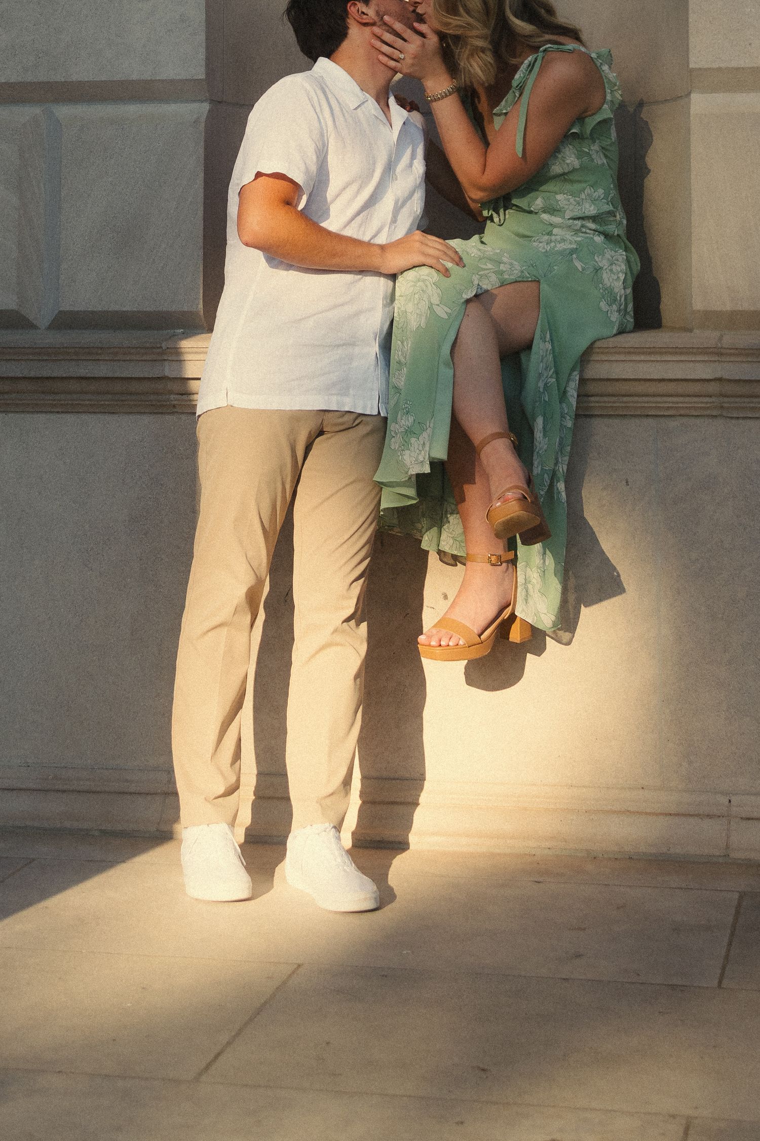 A romantic scene unfolds as two people in white and mint green attire dance together on a sunlit patio.