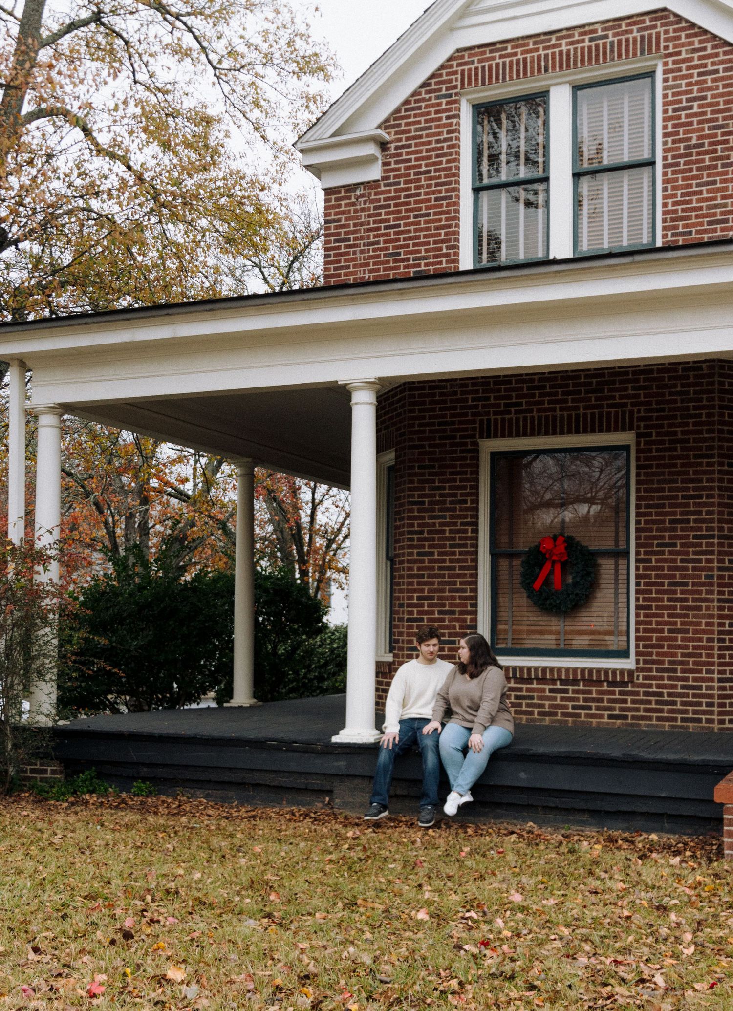 Long red brick ranch house with white trim and colonial-style pillars displays a holiday wreath in fall.
