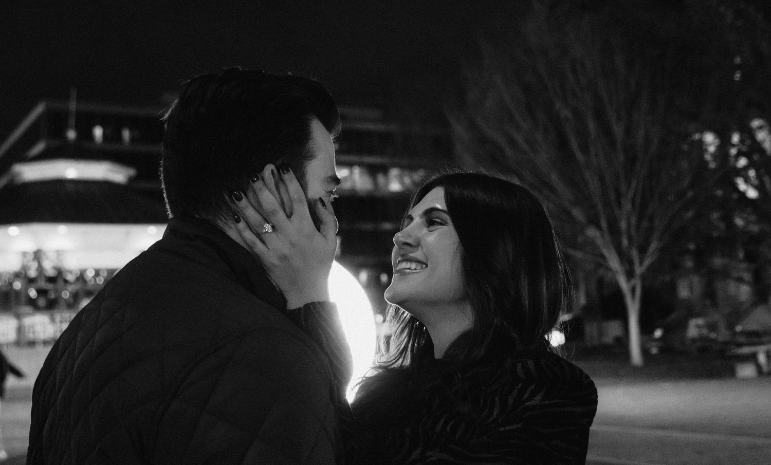 A romantic black and white nighttime scene of a couple sharing an intimate moment on a city street.