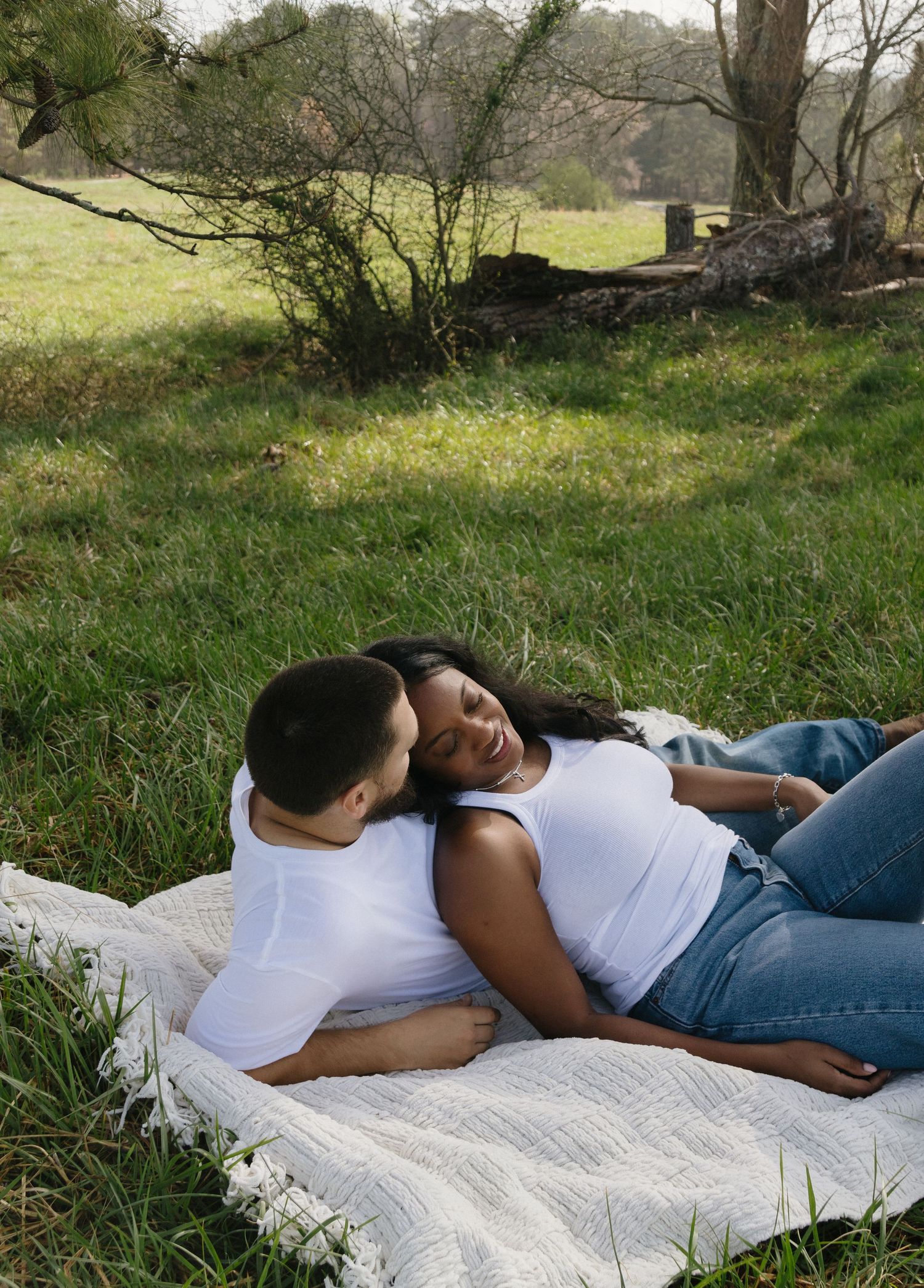 Two people share an intimate moment while relaxing on a blanket in a peaceful grass field on a spring day.