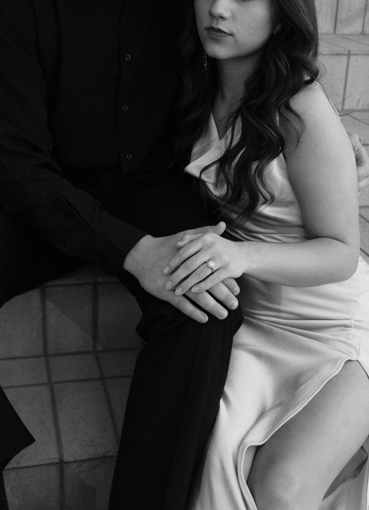 Black and white artistic photograph showing hands delicately embracing in shadow against a light background.