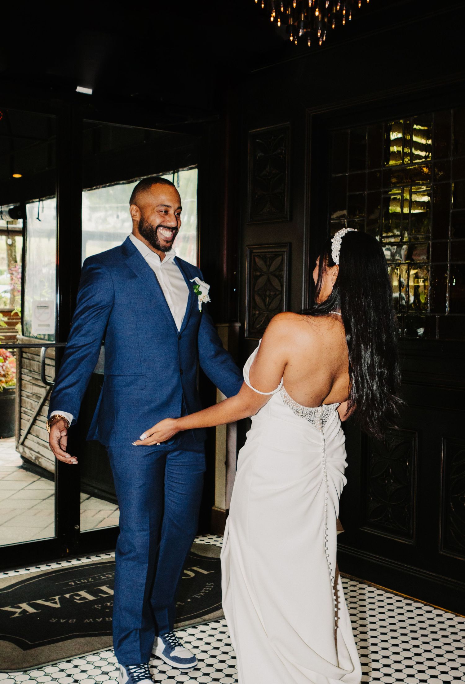 A wedding photo showing a couple in formal attire, with the groom wearing a blue suit and the bride in a backless white dress.