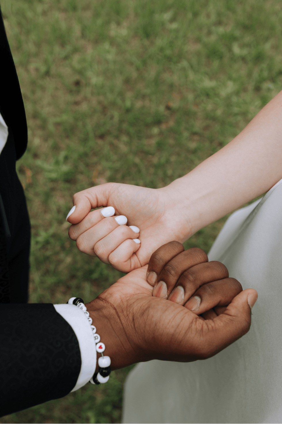 Two people hold hands intimately during a wedding ceremony, with one wearing white lace and the other in black attire.