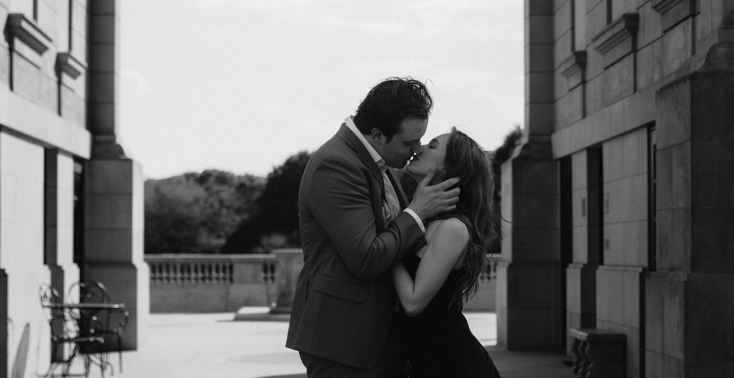 A romantic black and white photograph showing a couple sharing a tender embrace on a balcony.