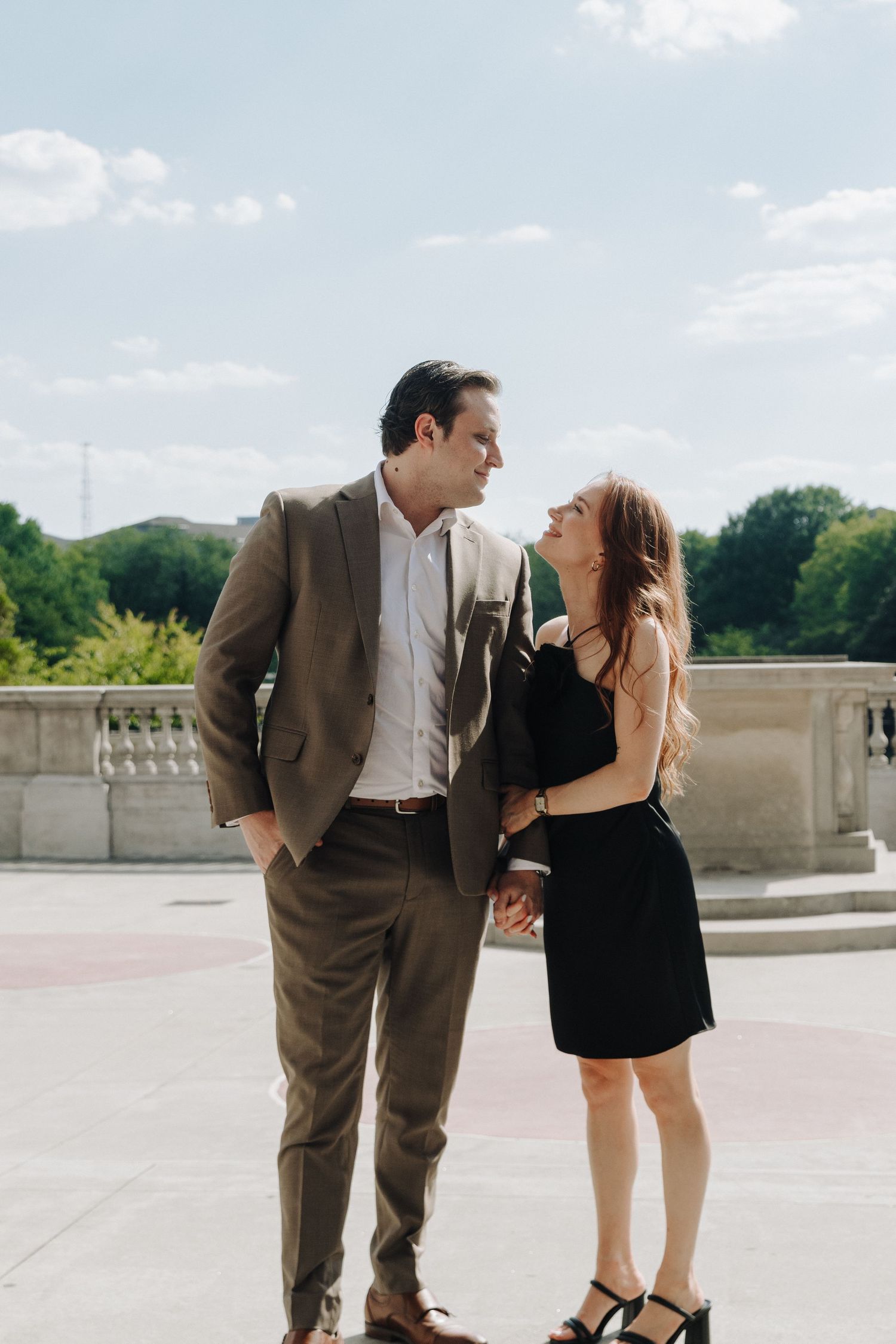 A couple shares a playful moment together outdoors on a stone terrace under a bright blue sky.