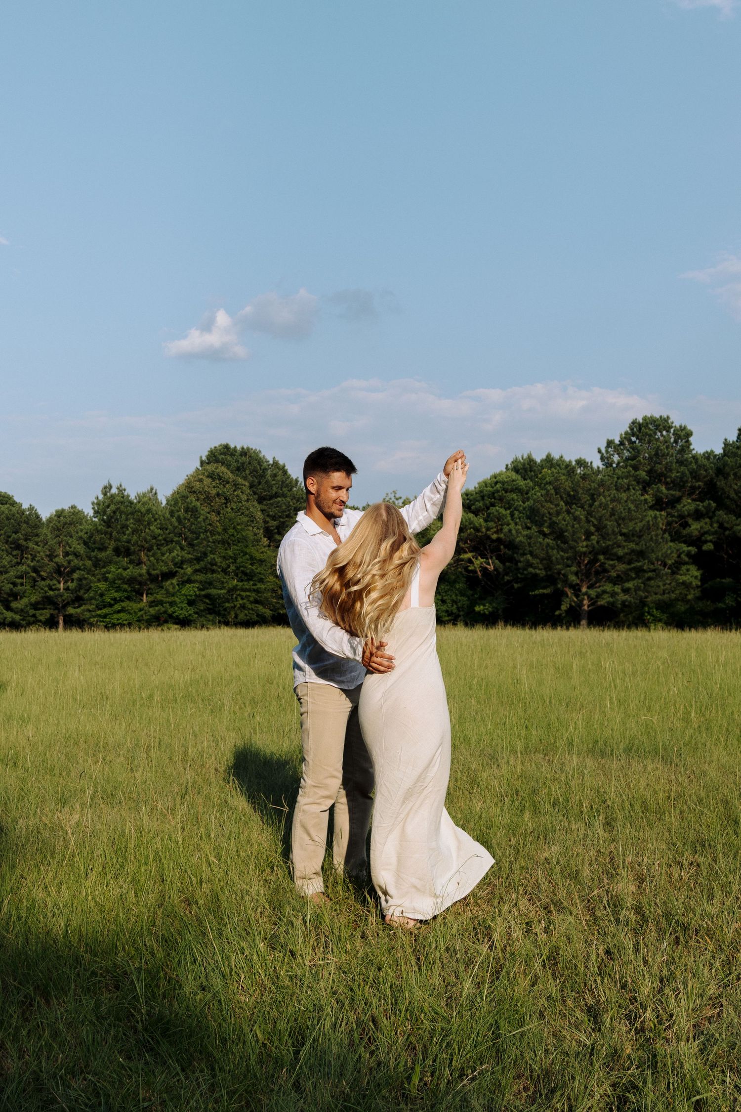 A couple share an intimate dance moment in a sun-lit meadow with tall grass and trees in the background.