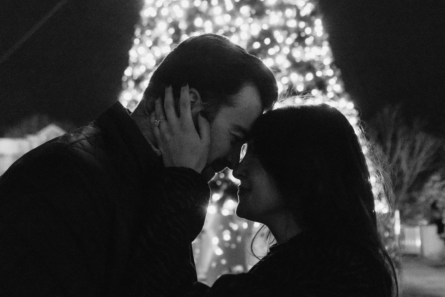 A romantic silhouetted couple shares a tender moment while sitting together in a park setting at sunset.