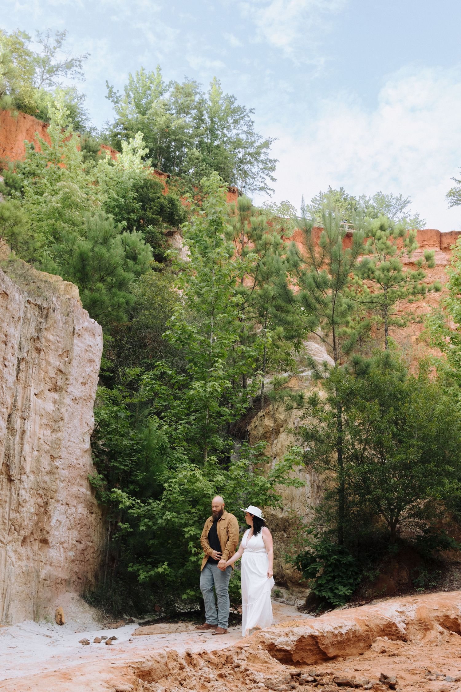 Rocky outdoor climbing wall surrounded by green trees with people practicing rock climbing techniques in natural setting.