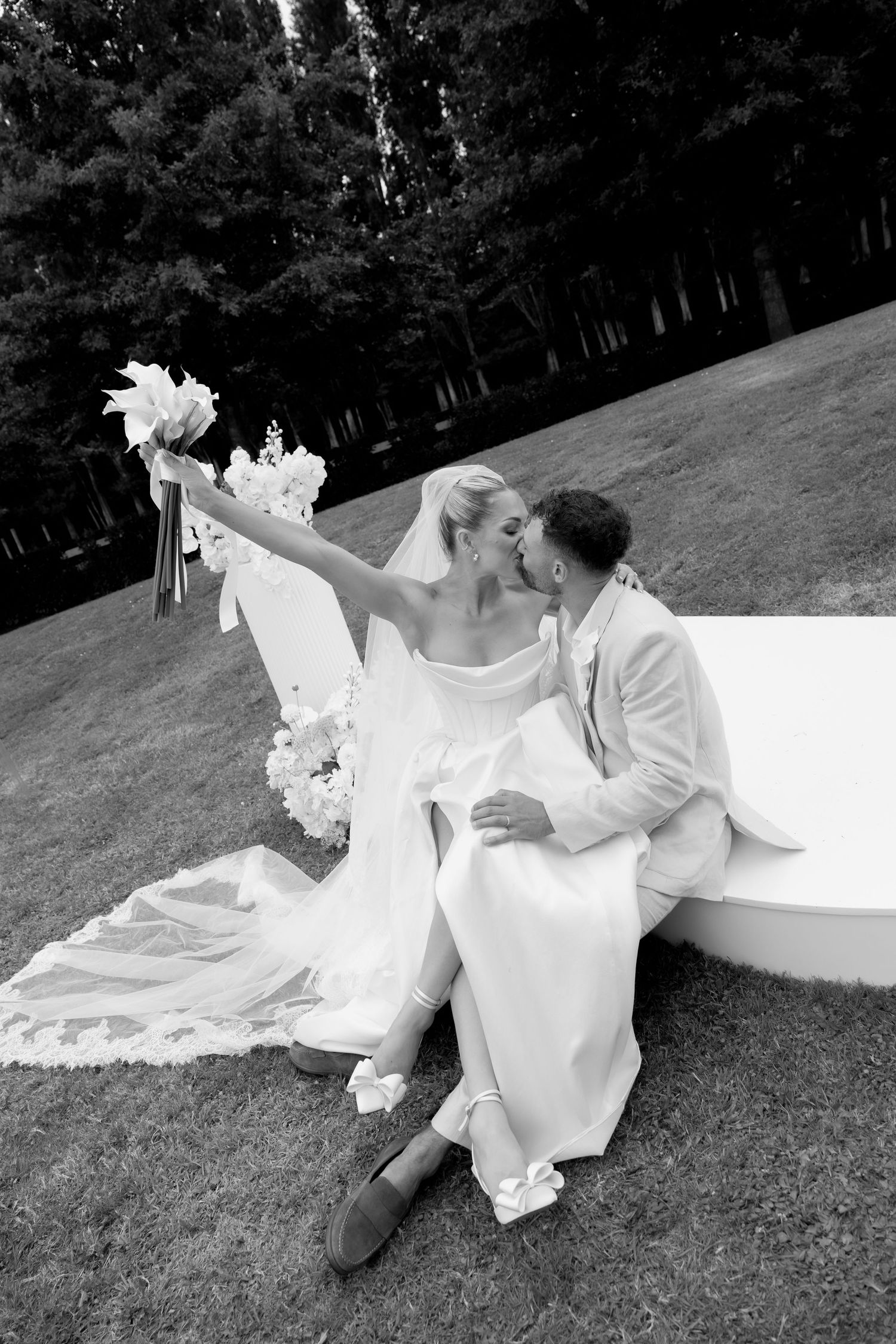 A romantic black and white photo sequence of a couple lying on grass with a flowing white dress creating movement.