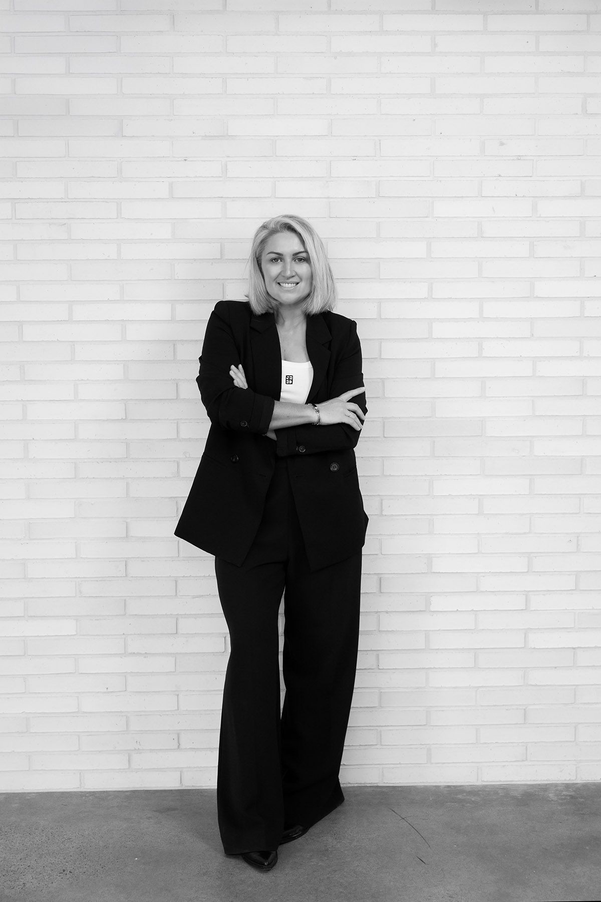 Professional black and white portrait series of a woman in business attire posing against a white brick wall.