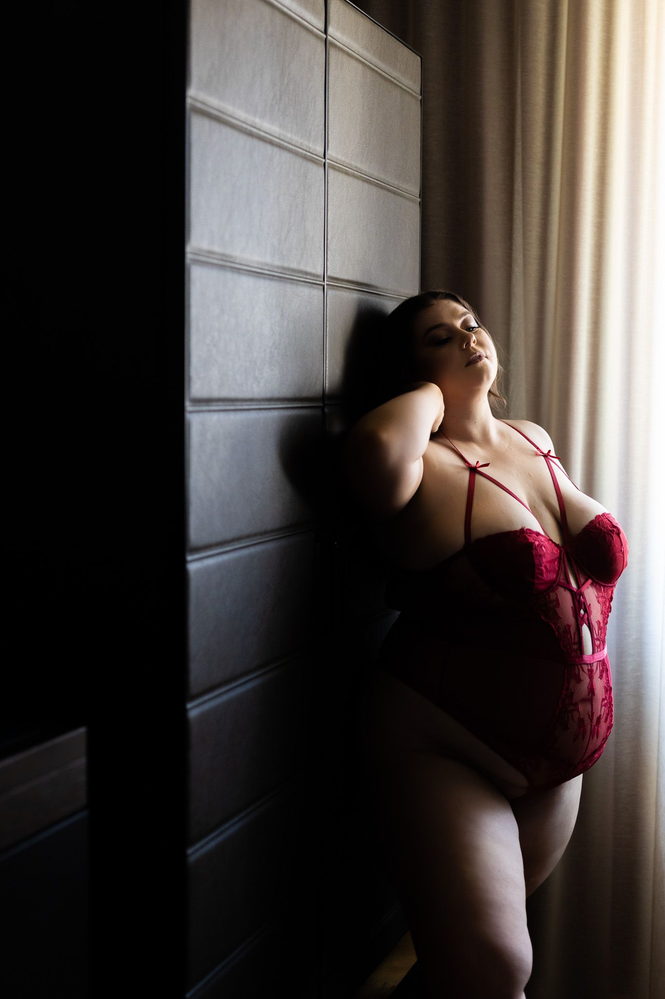 Artistic boudoir photography with dramatic window lighting and shadows against a modern paneled wall.