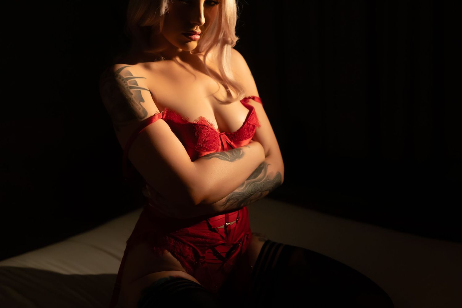 Person in red lingerie poses against dark background with dramatic lighting and shadows.