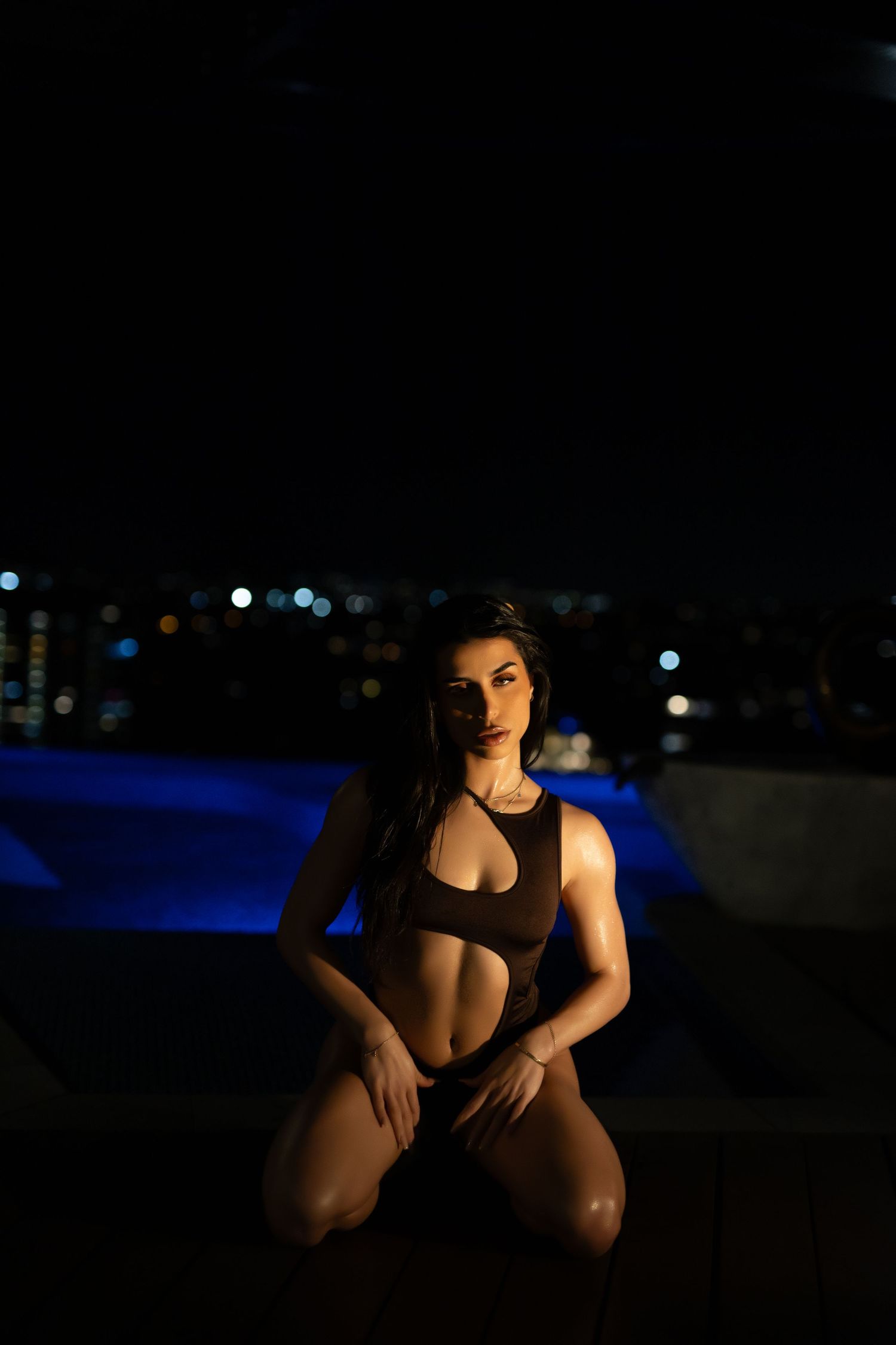 Silhouetted figure in black attire poses dramatically against dark background with bokeh lights.