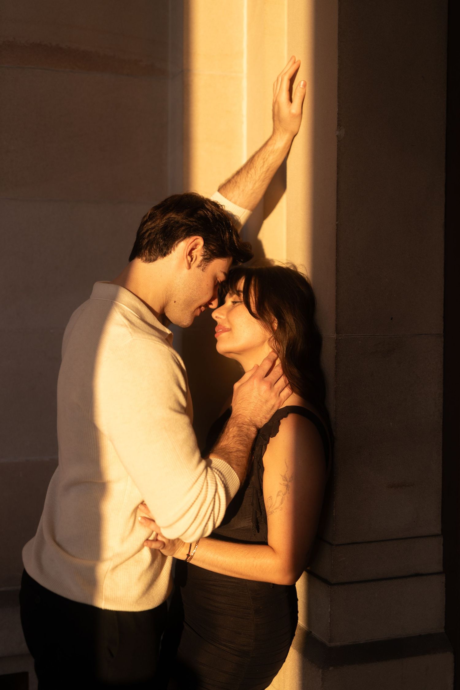 Two people in dramatic lighting embrace against a wall creating stark shadows in an intimate scene.
