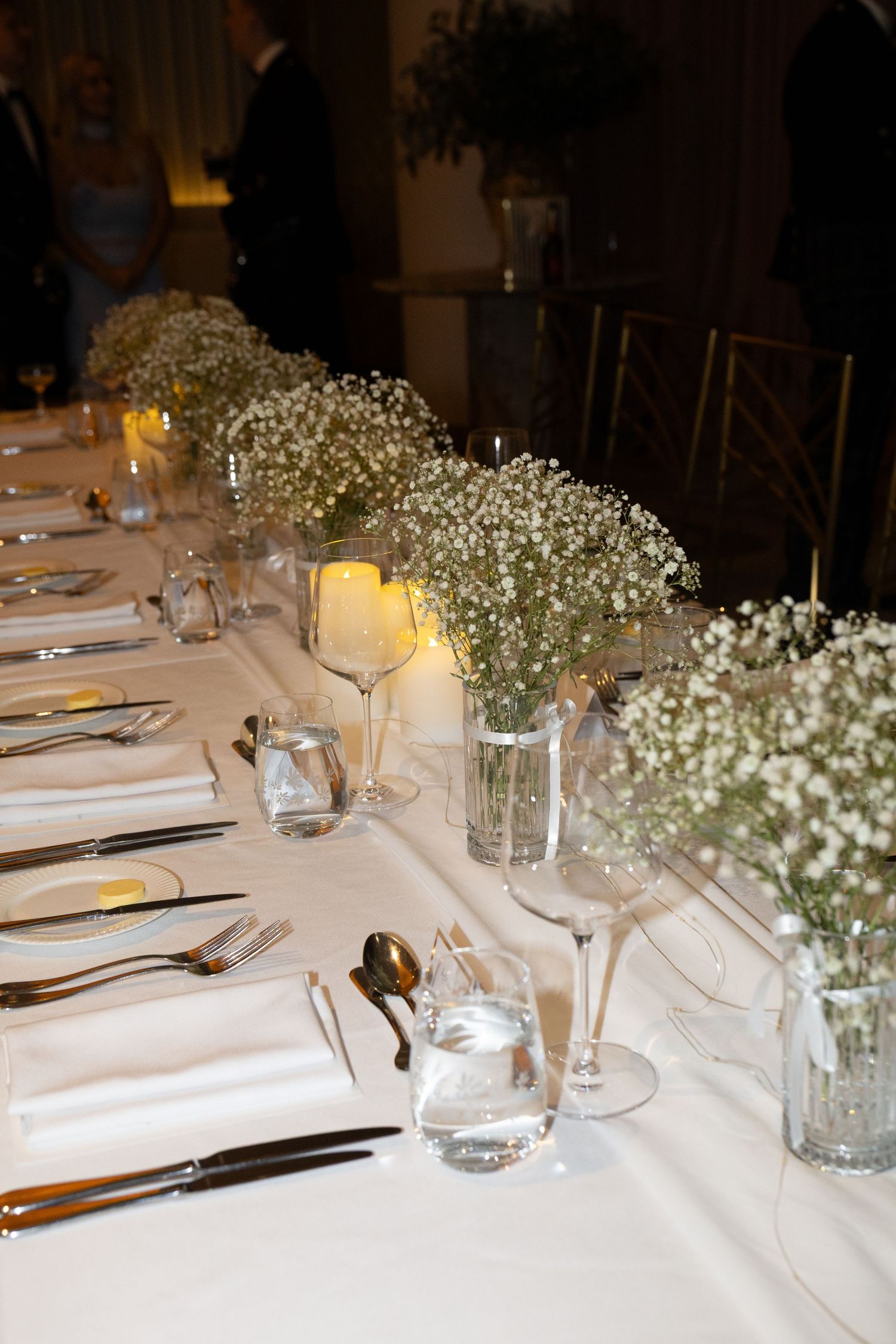 Elegant wedding reception table with baby's breath floral centerpieces, white linens, candles, and formal place settings.