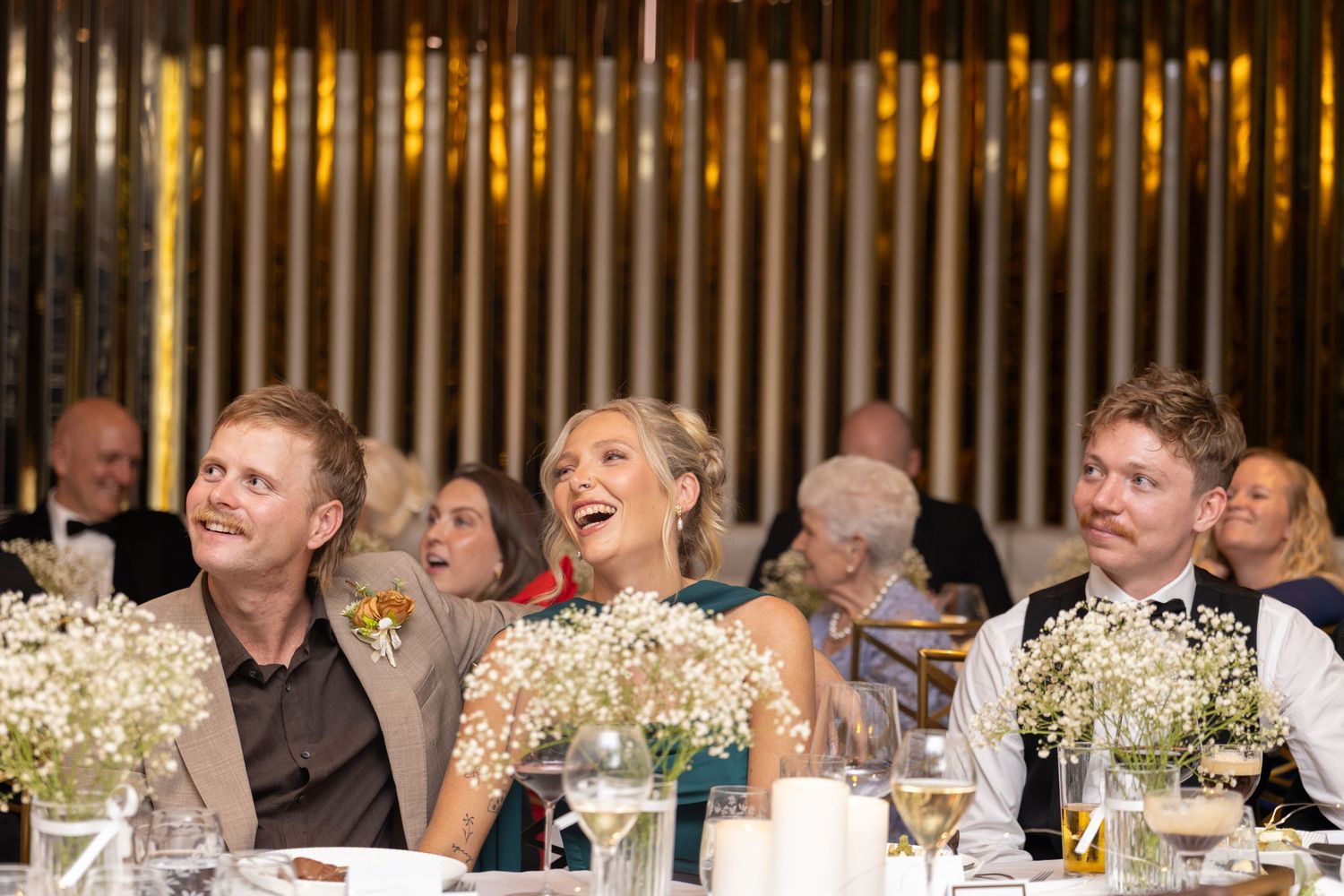 Bride and groom laughing joyfully at wedding reception table adorned with baby's breath floral arrangements.