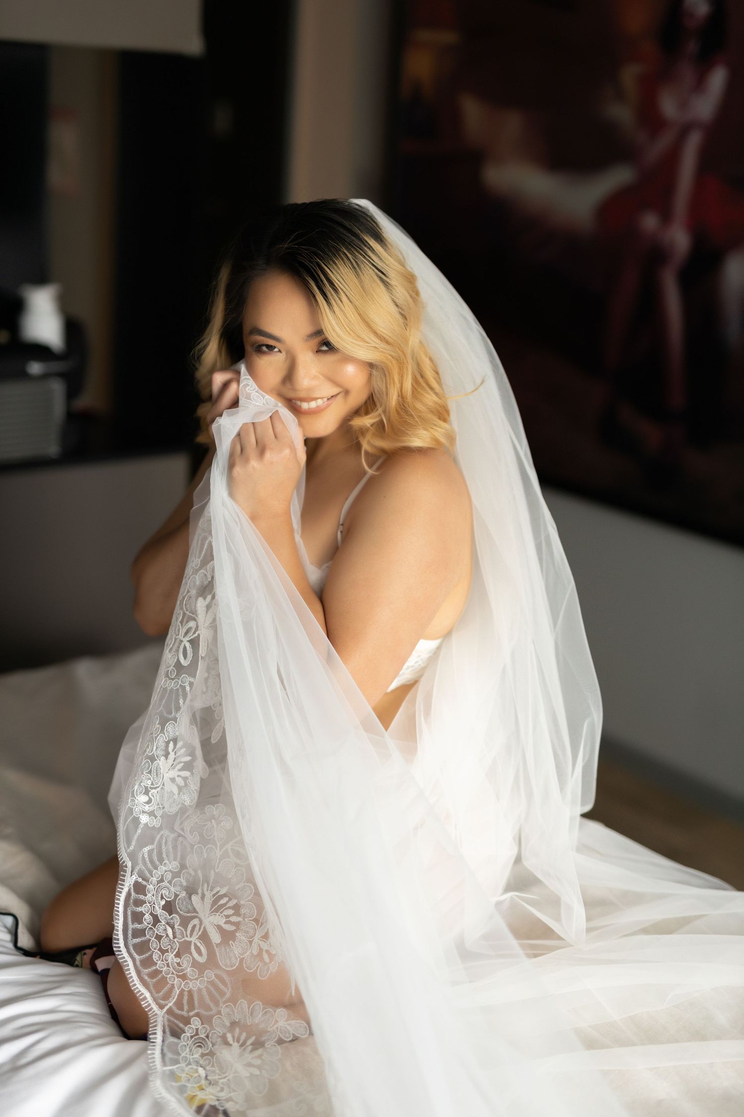 A bride in a white wedding dress and veil poses for a series of romantic boudoir photos.