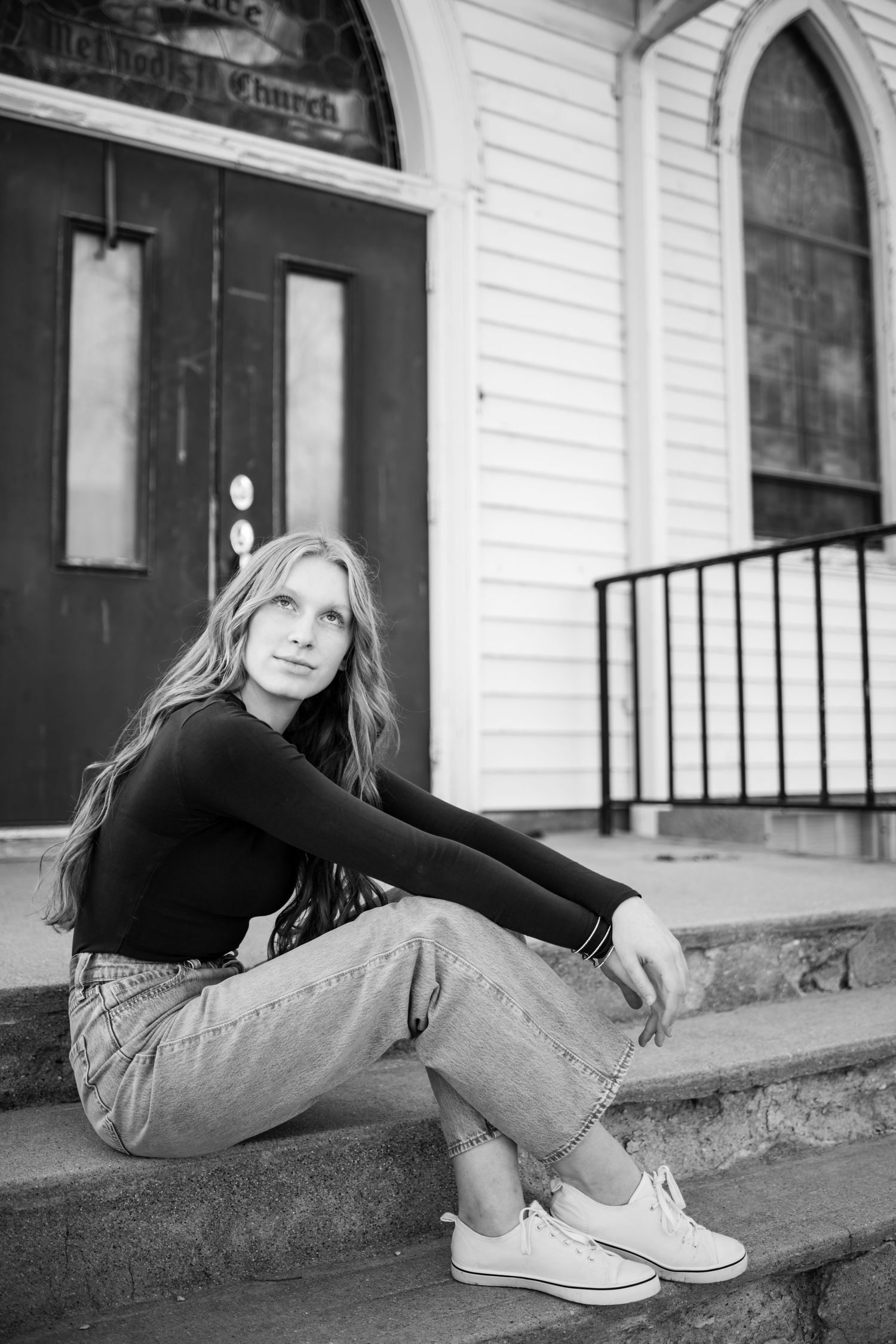 Blonde teen girl sitting on church steps in black turtleneck and jeans in black and white.