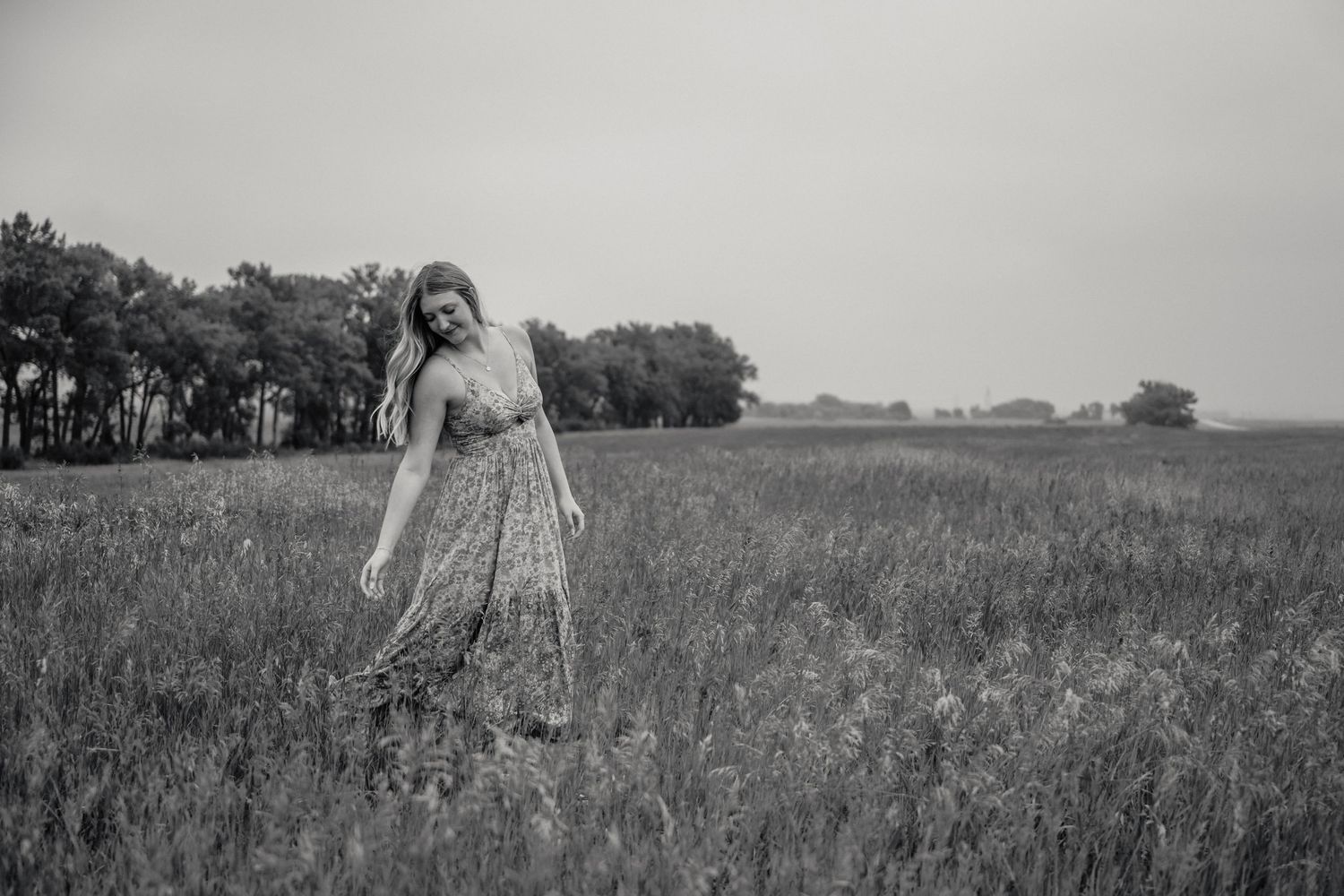 Woman in floral maxi dress walking through open field in black and white portrait.
