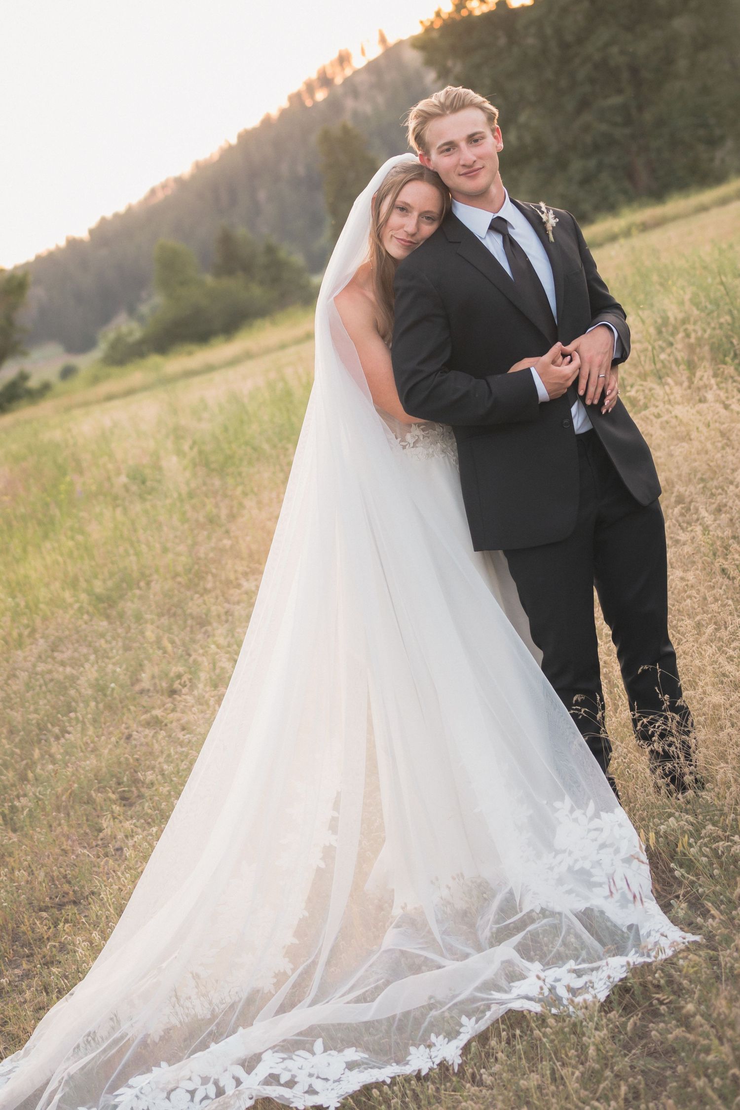 Bride and groom embracing in golden sunset light in a grassy mountain meadow on wedding day.