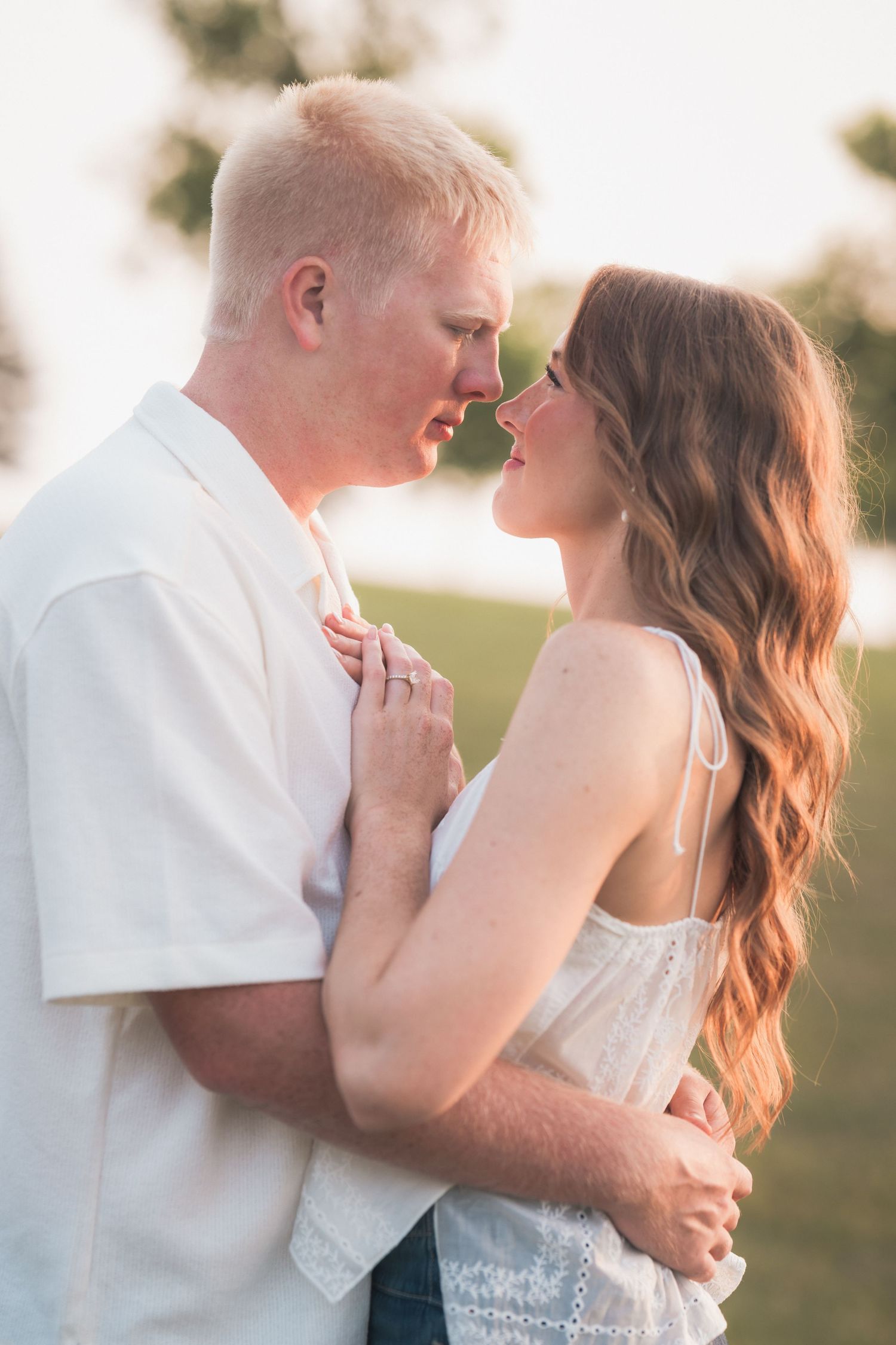 Couple sharing a romantic moment outdoors, woman in white lace dress with auburn hair, man in white t-shirt, golden hour light.