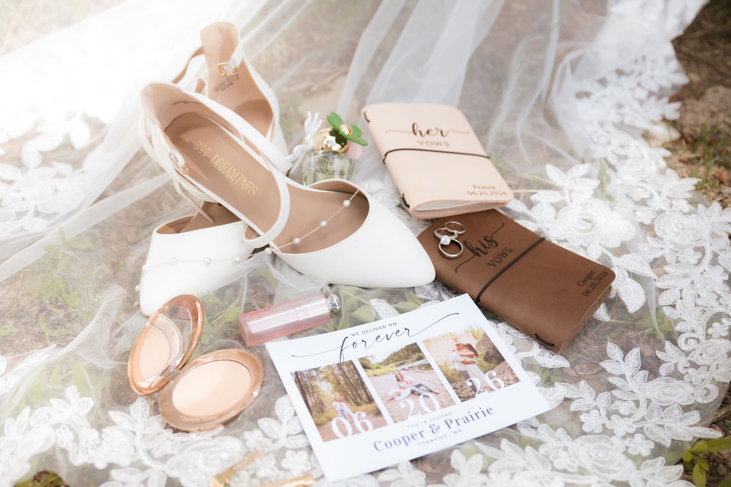 Flat lay of wedding details including heels, rings, vow books, and invitation on lace veil.