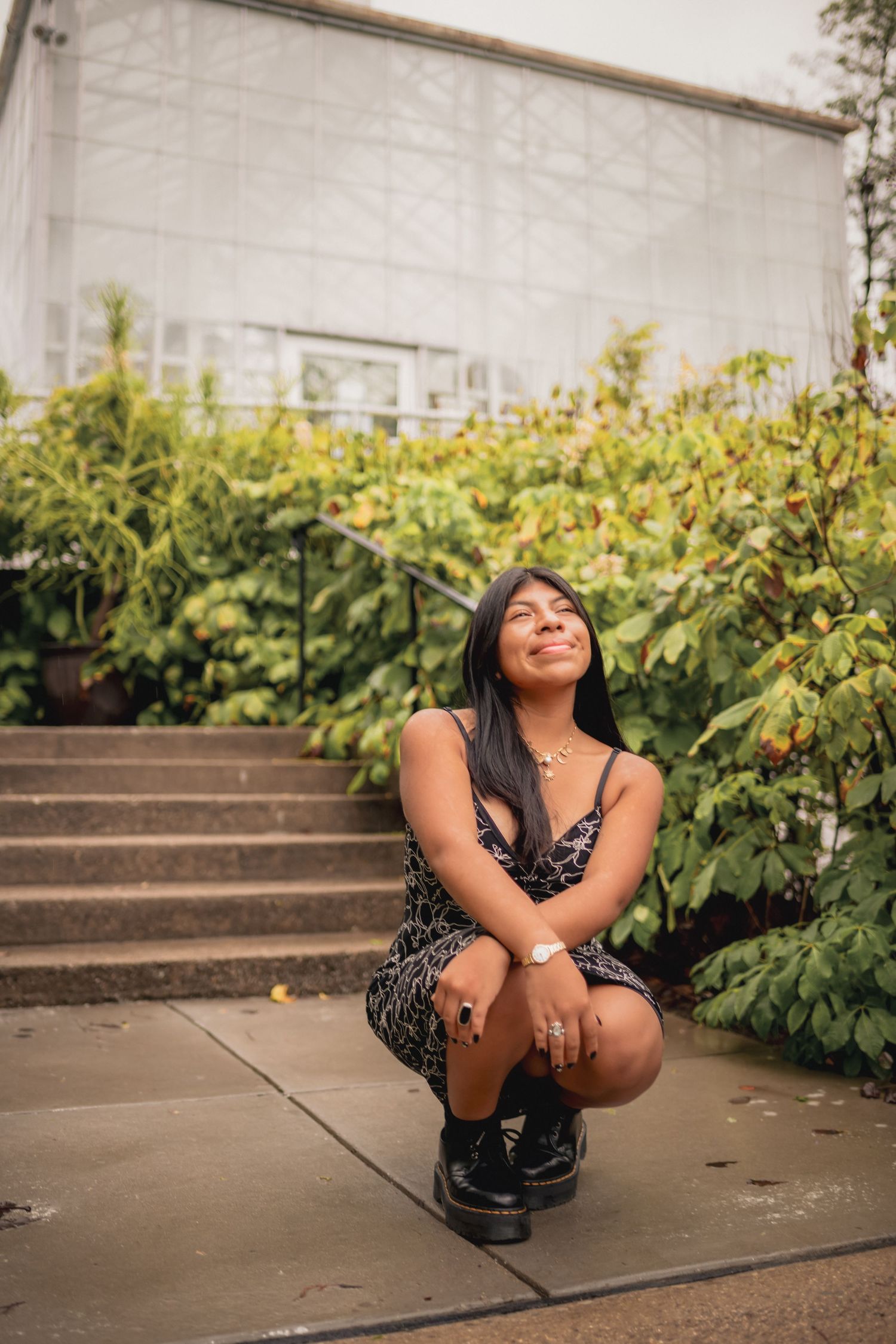 Young woman in leopard print dress smiling upward while crouching near greenhouse steps in Cincinnati, OH.