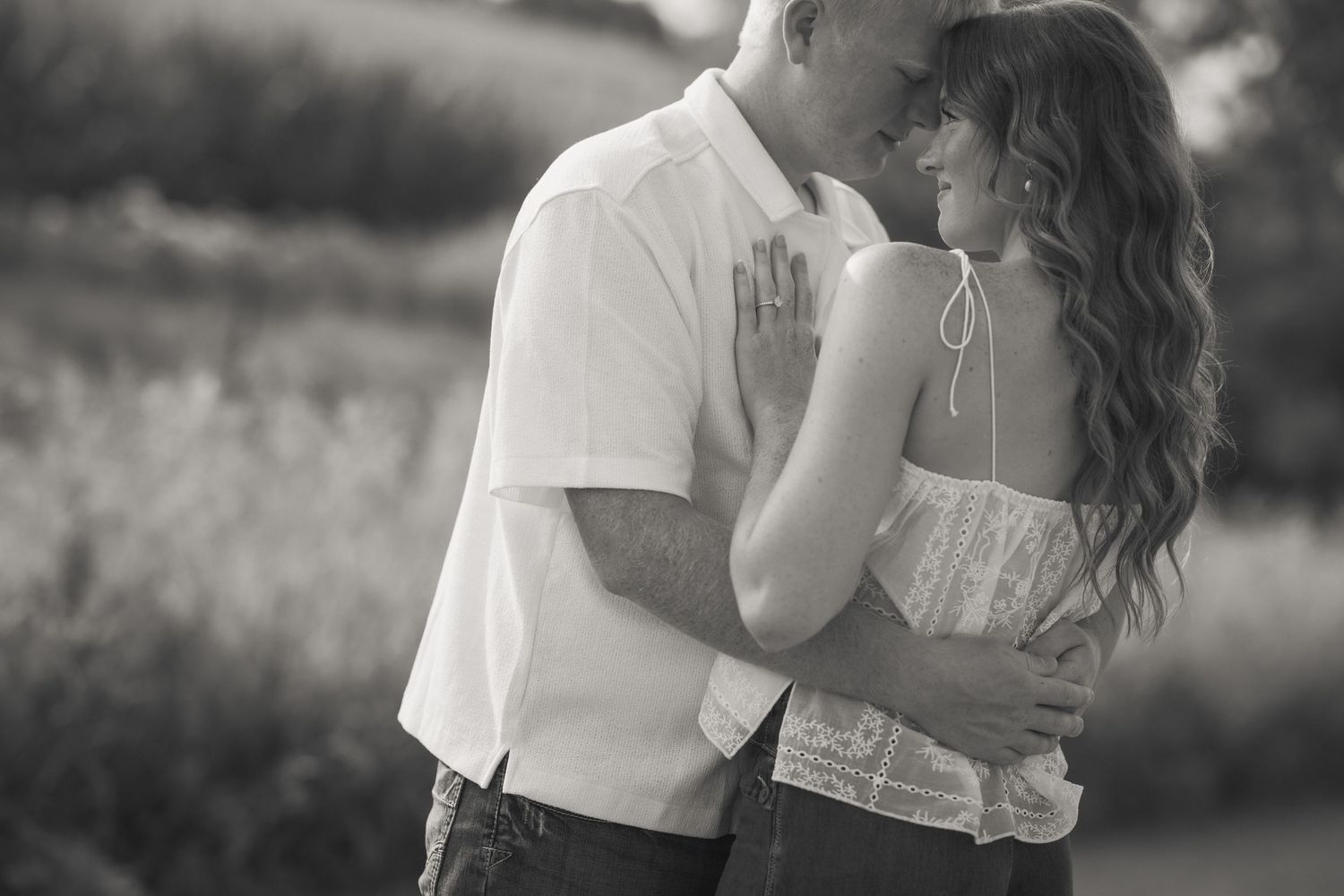 Black and white photo of a romantic couple embracing outdoors, woman in white top resting hand on mans chest.