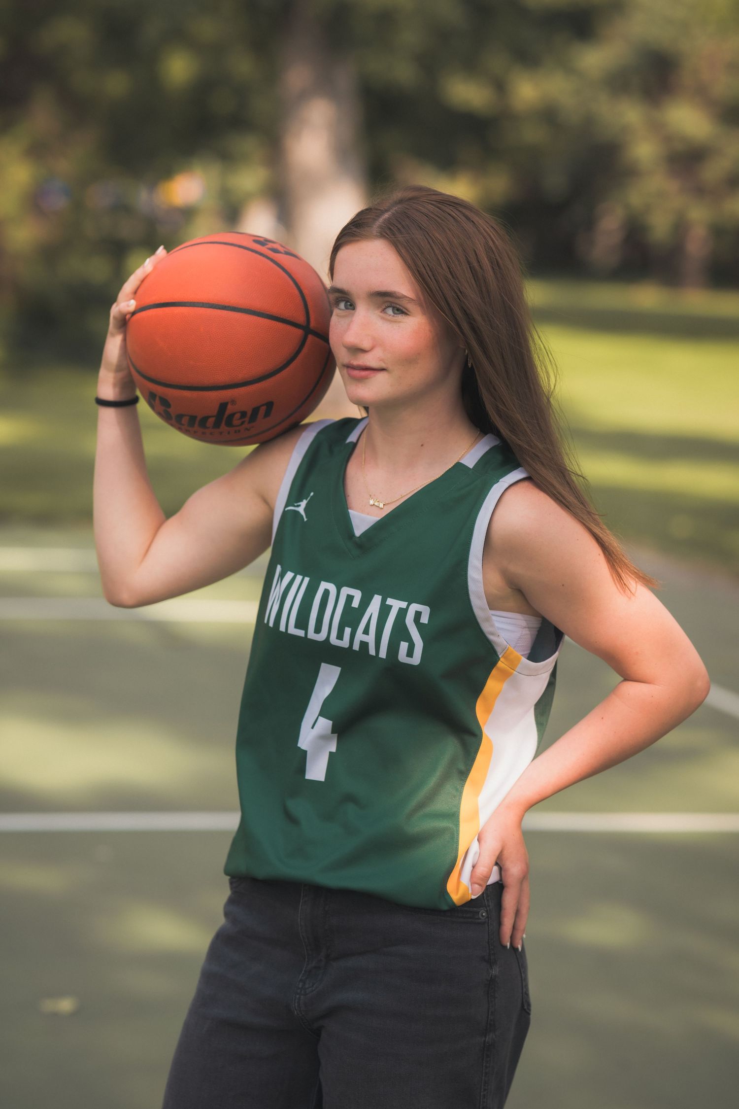 Young woman in green Wildcats #4 basketball jersey holding a ball on an outdoor court.