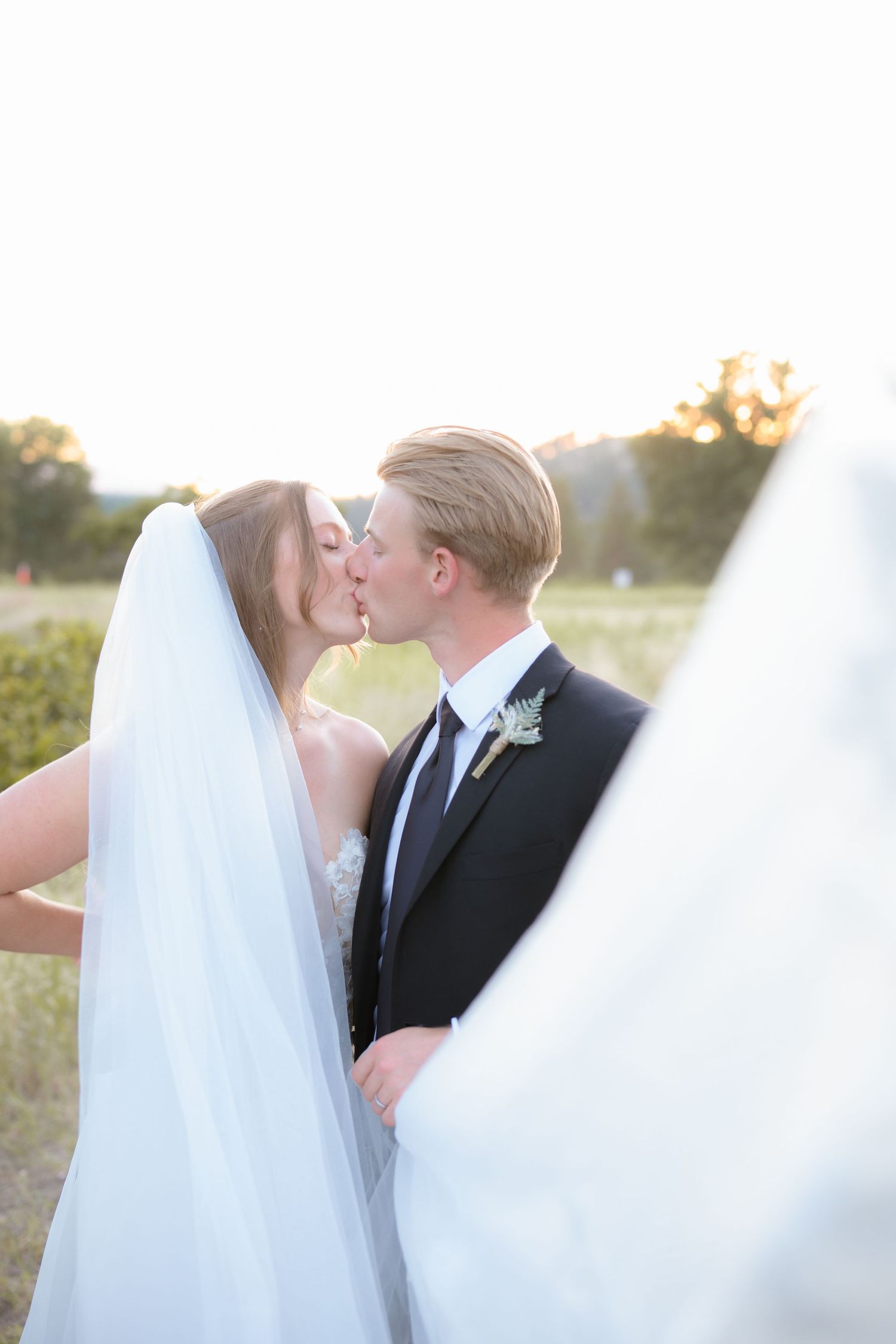 Bride and groom sharing a kiss at sunset with flowing veil in the foreground on wedding day in the PNW.
