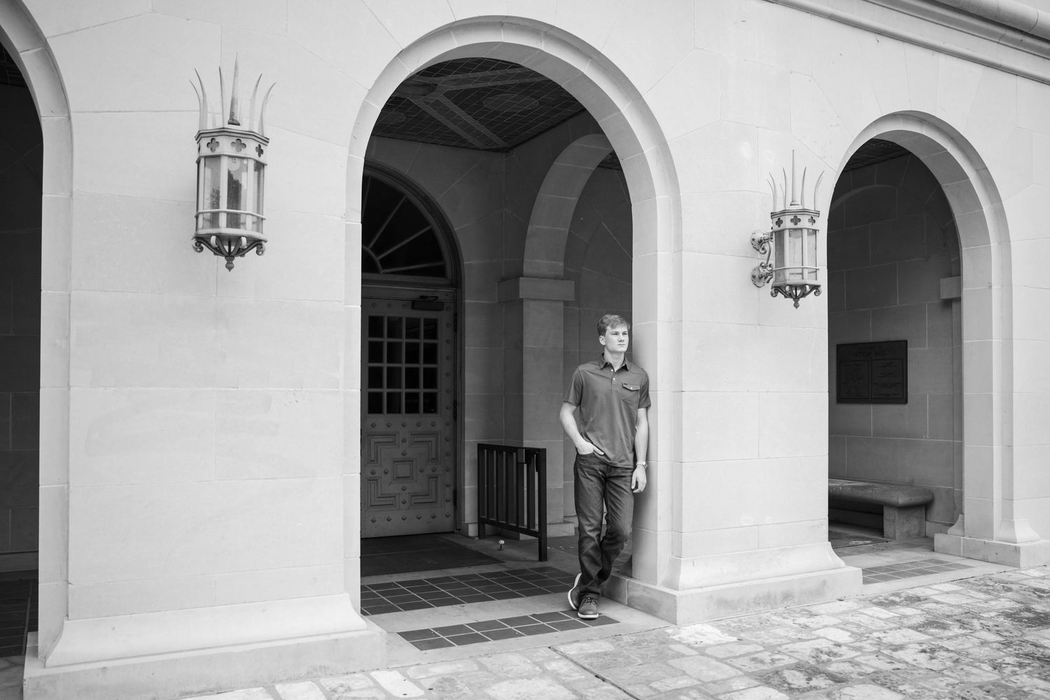 Young man leaning against archway column in black and white architectural portrait at University of Texas campus.