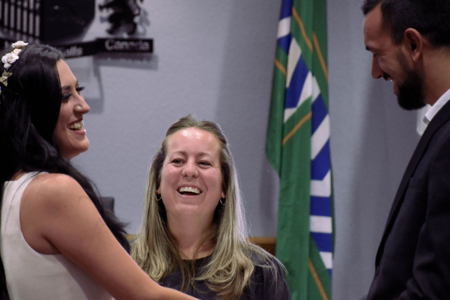 Couple and officiant sharing a laugh during wedding ceremony in council chambers at Niagara Falls City Hall