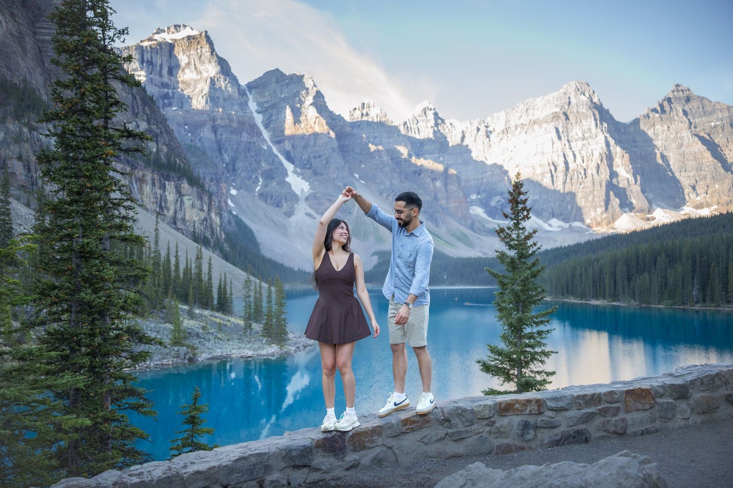 Couple dancing by turquoise Moraine Lake with snow-capped Rocky Mountains and evergreen trees in Banff, Canada.