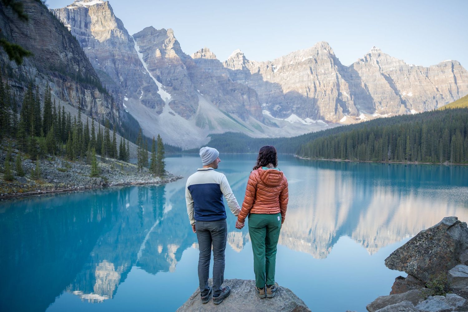 Couple holding hands at Moraine Lake, Banff, with turquoise water and Rocky Mountain peaks reflected in calm waters.