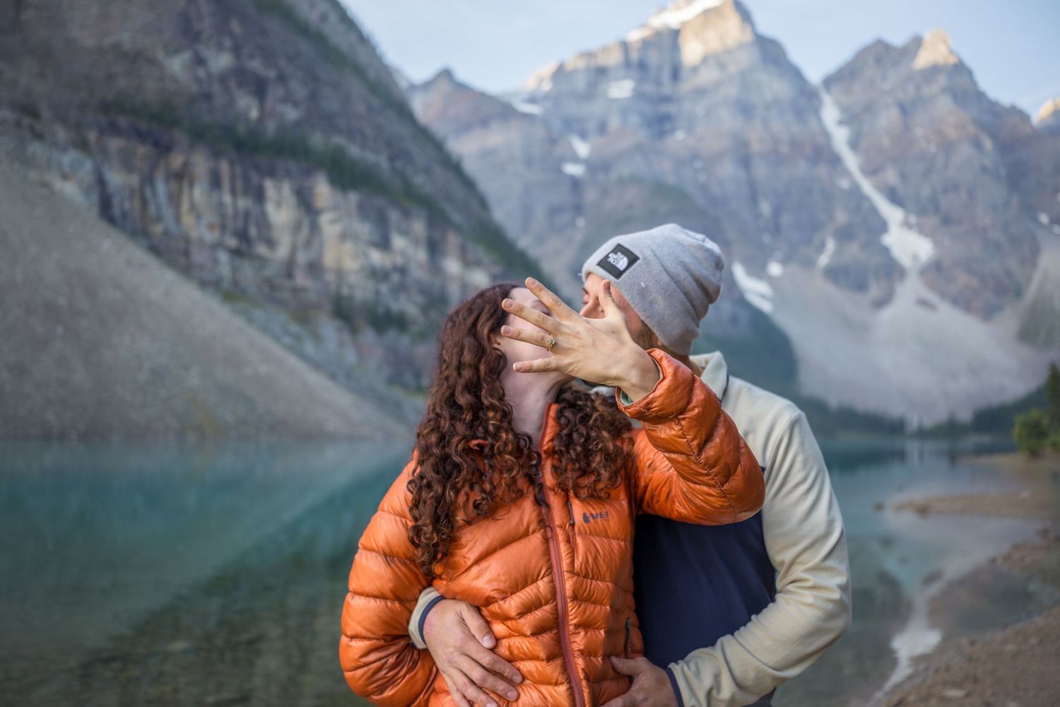 Couple sharing a kiss at Moraine Lake with stunning Rocky Mountain peaks and turquoise water in Banff, Canada.
