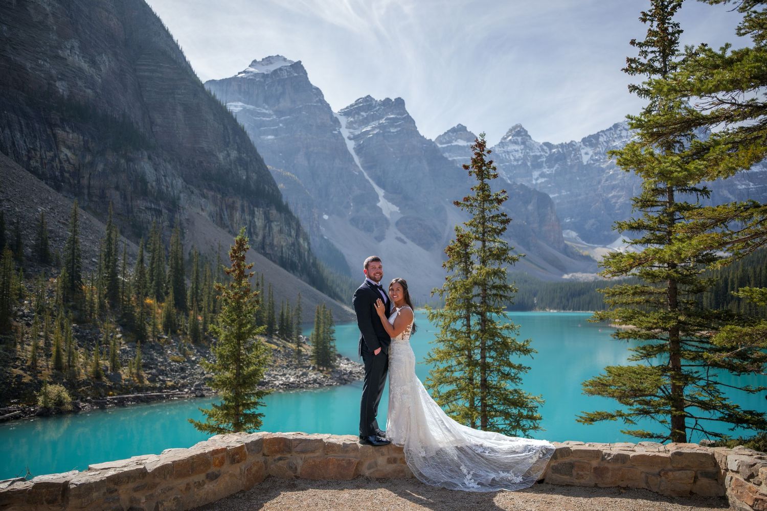 Bride and groom pose at Moraine Lake, Banff, with turquoise water and Rocky Mountain peaks backdrop.