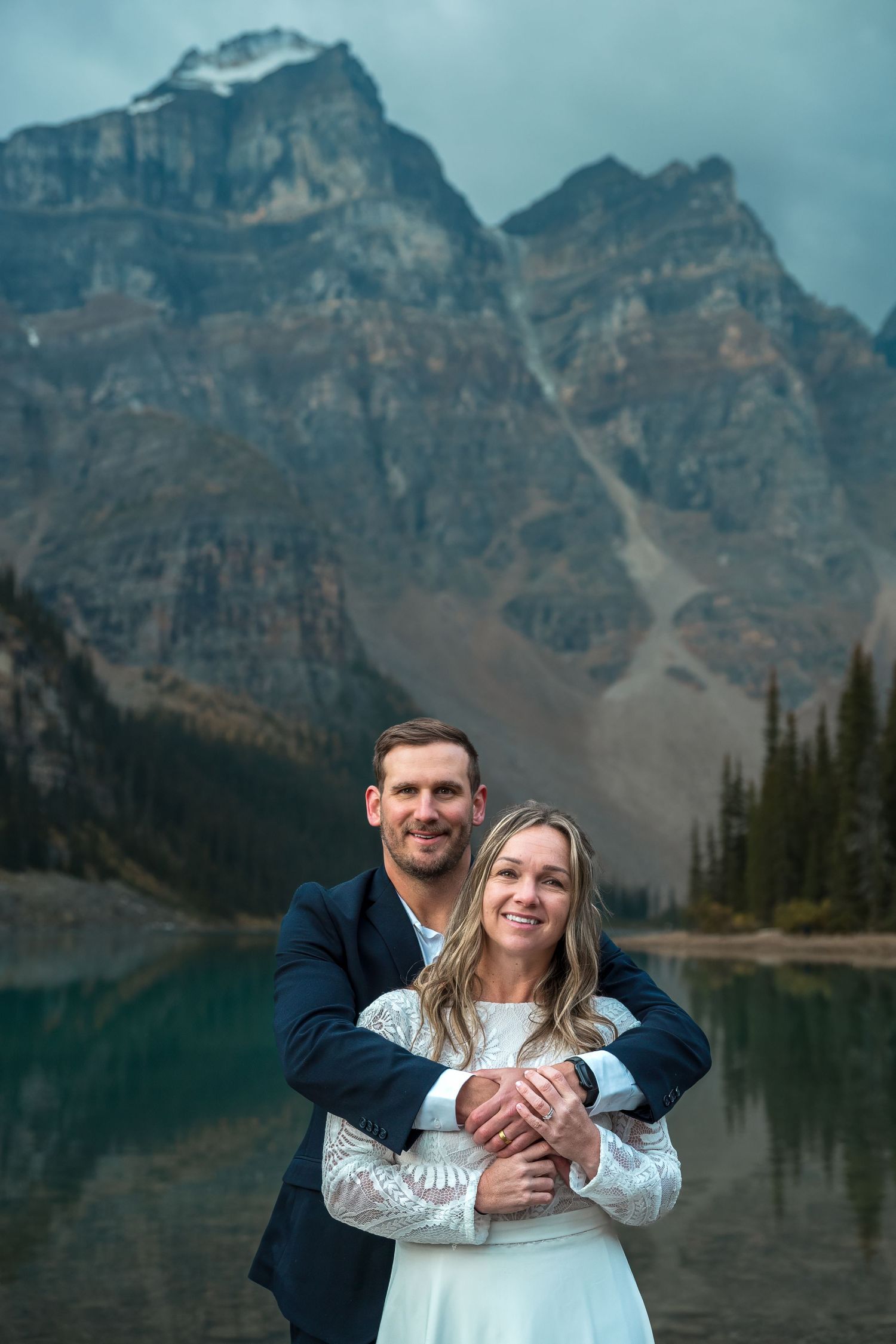 Couple embracing in front of Moraine Lake with dramatic Rocky Mountain peaks in Banff, Canada.