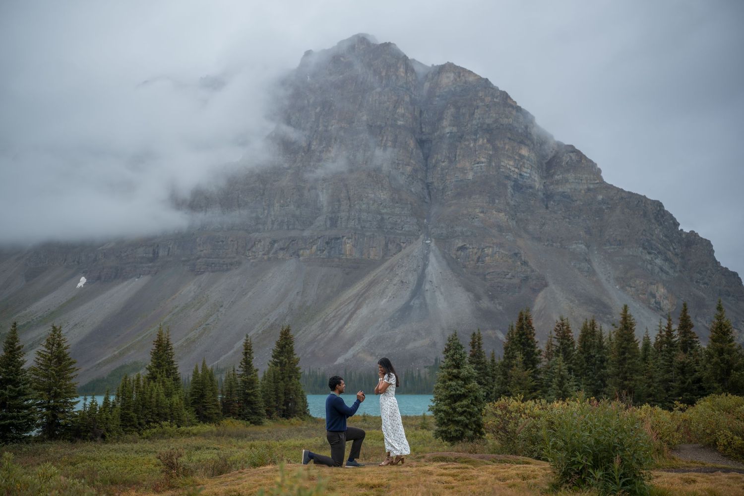 Couple's mountain proposal at Bow Lake in Banff, man on one knee before stunning rocky peaks and turquoise water.