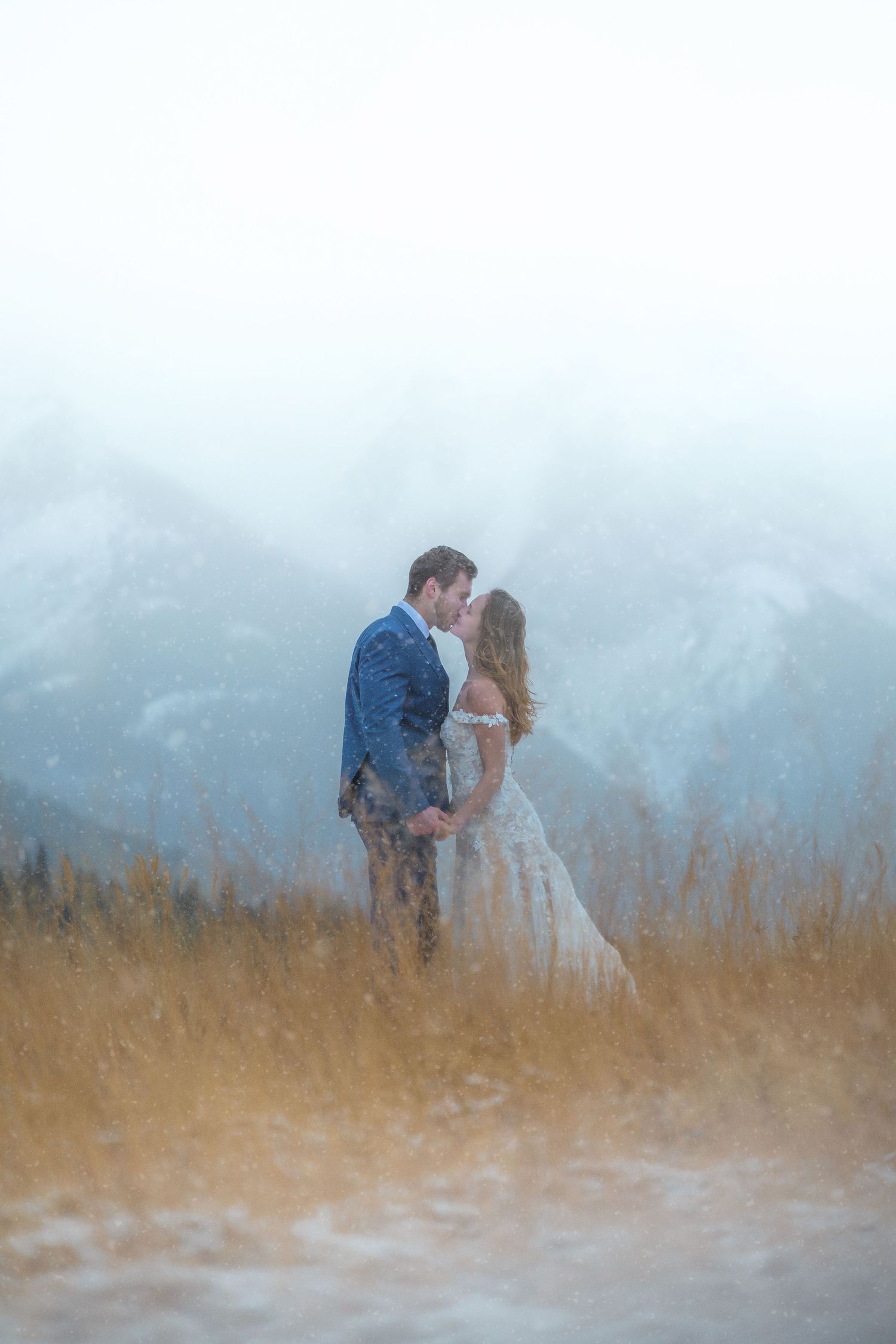 Bride and groom kissing in snowy mountain meadow during a romantic winter elopement in the Rockies.