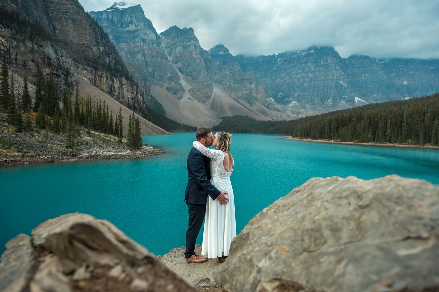 Bride and groom sharing a kiss at Moraine Lake with vibrant turquoise water and mountains behind them.