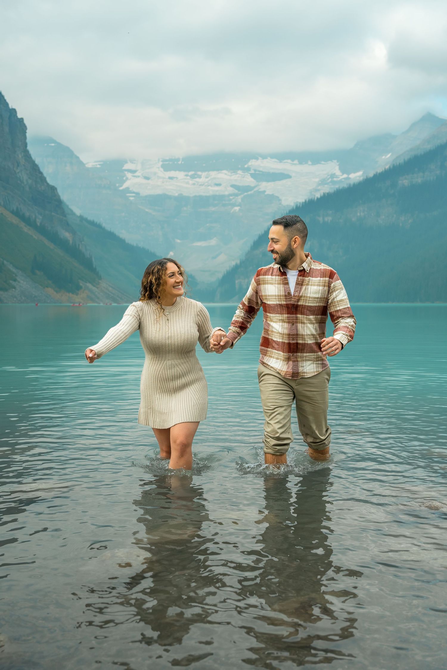 Happy couple holding hands and wading through the glacial turquoise waters of Lake Louise, Alberta.