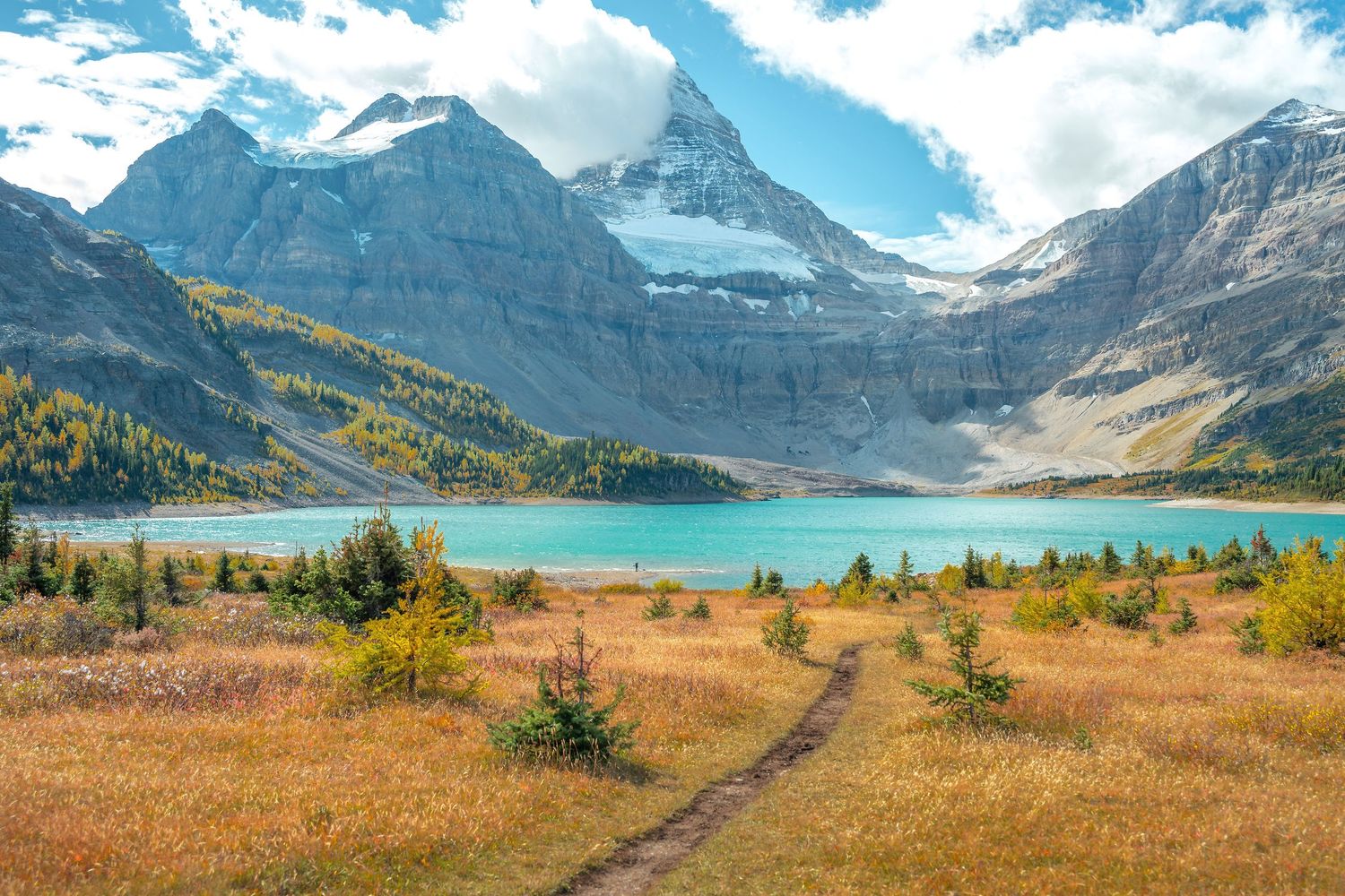Stunning turquoise alpine lake with dramatic snow-capped mountain peak and colorful autumn foliage in Canadian Rockies.