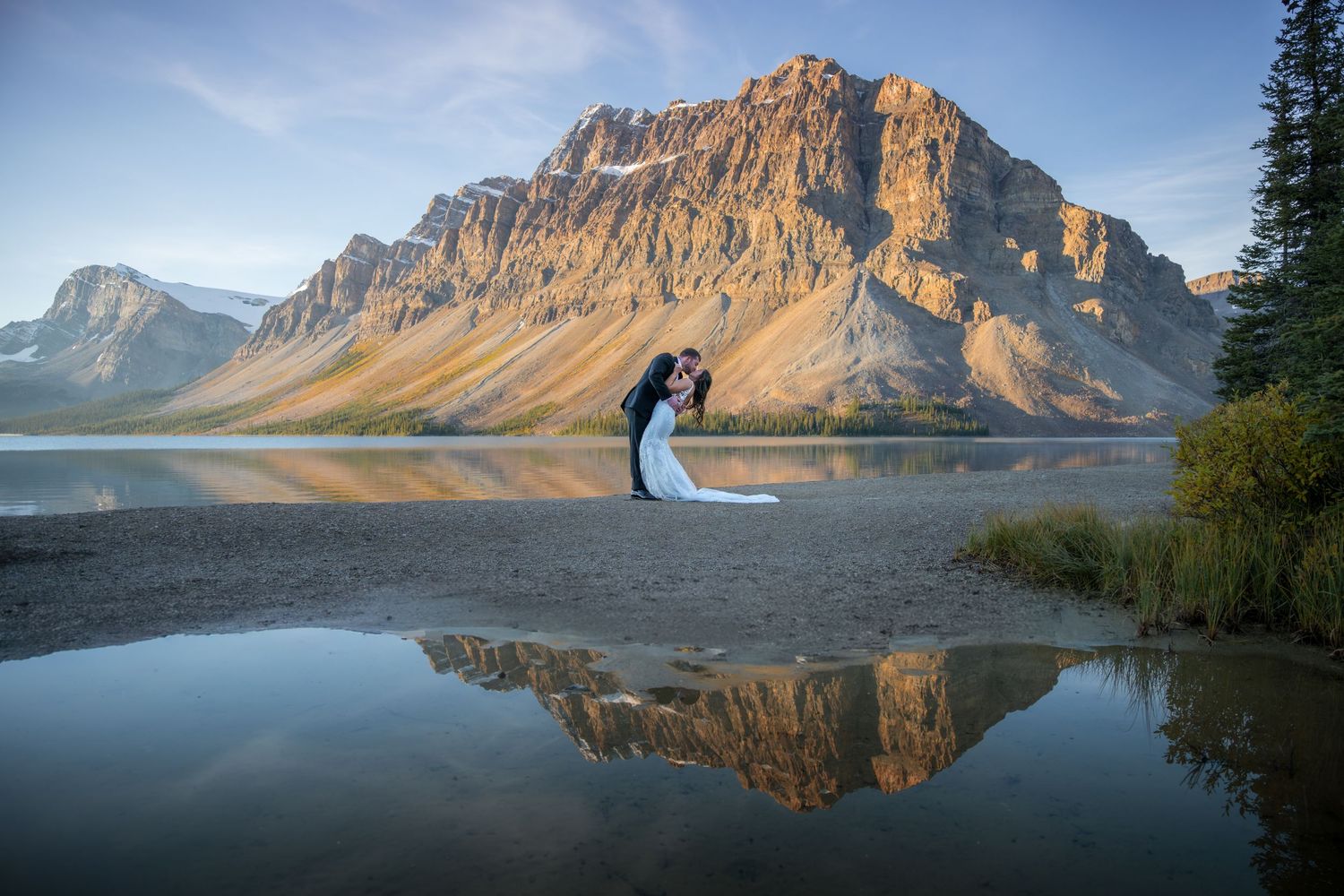 Couple sharing a kiss by a mountain lake with stunning reflections in Banff National Park on their wedding day.